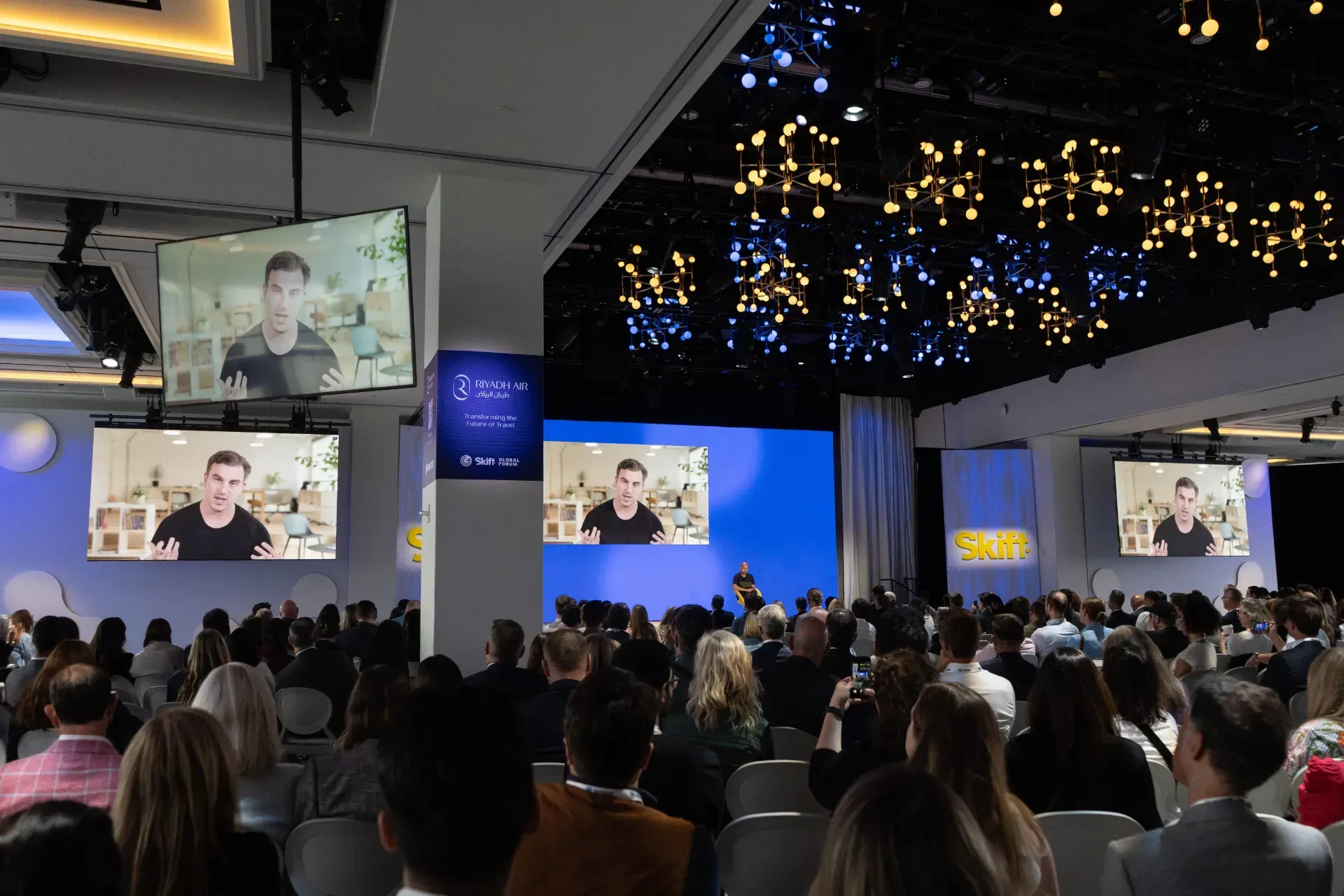 A large group of people are sitting in front of a large screen watching a presentation.