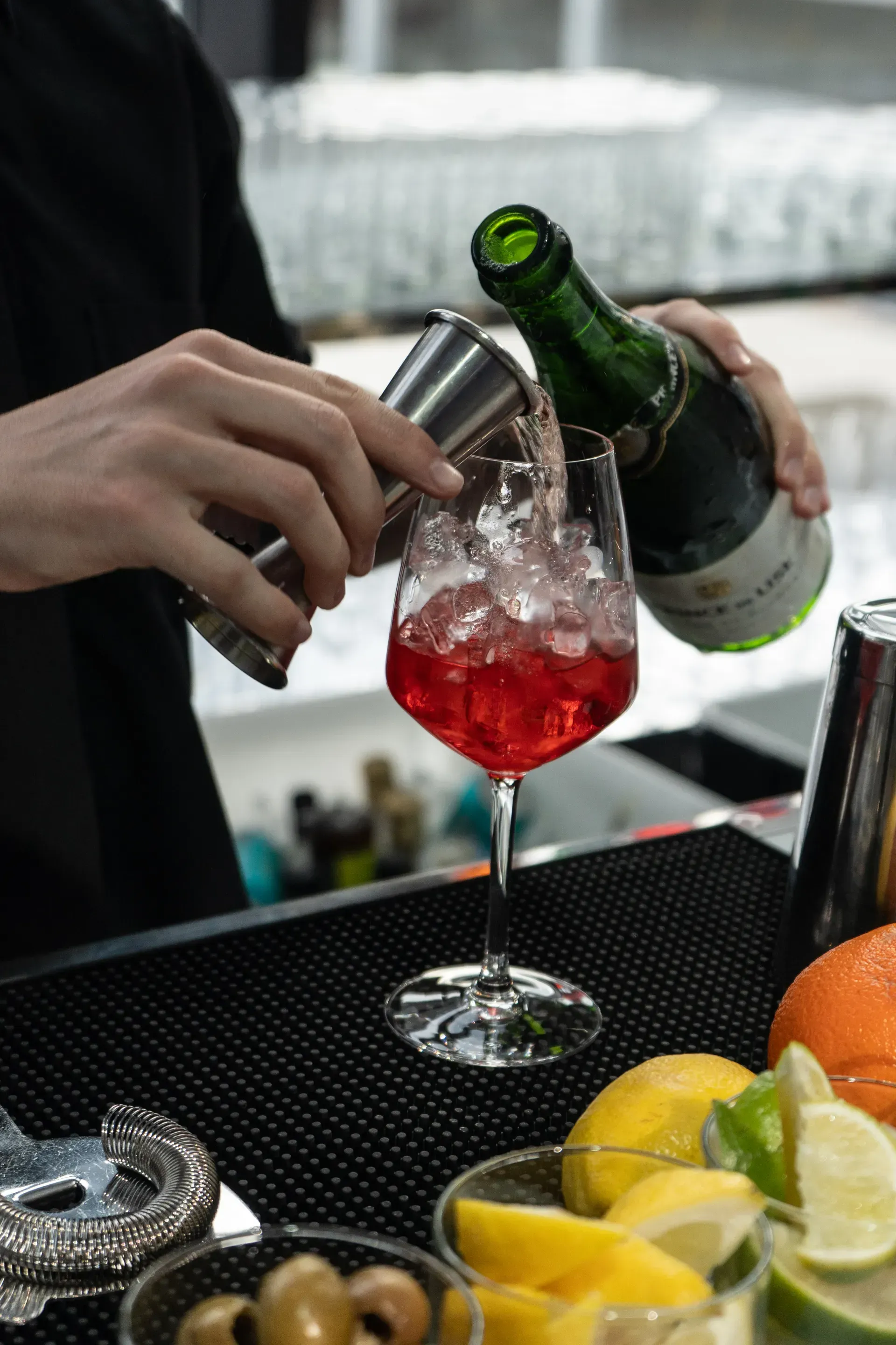A bartender is pouring a drink into a glass with ice.