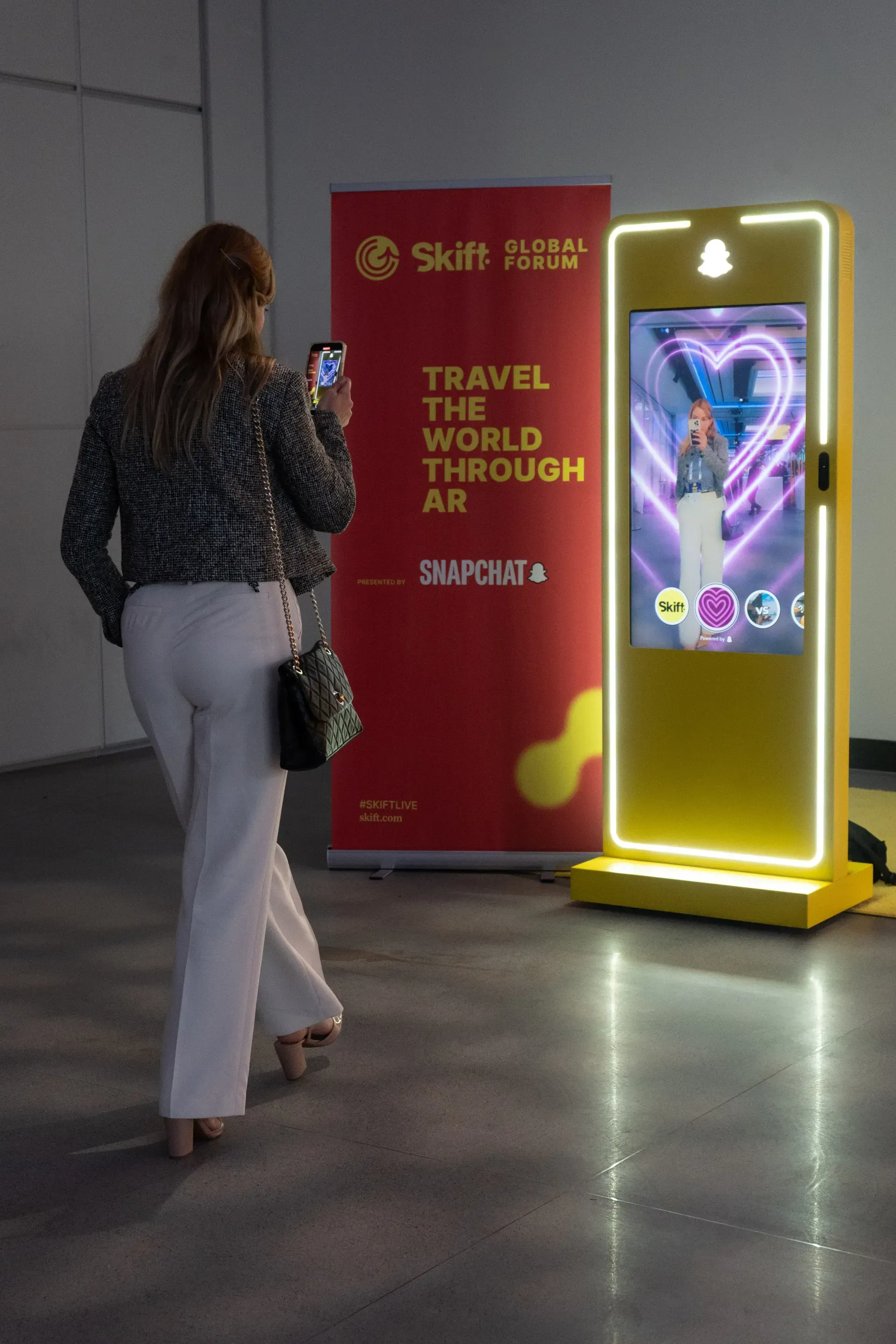 A woman is taking a picture of herself in front of a sign that says travel the world through ar