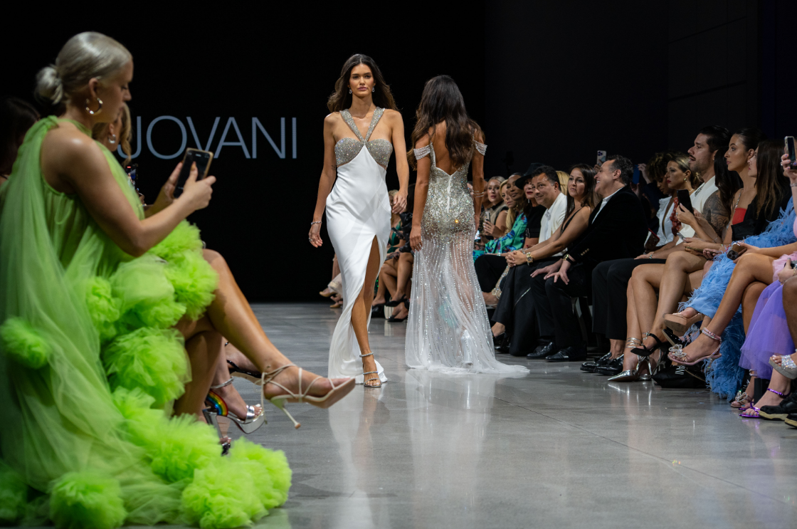 A woman in a green dress is sitting on the runway at a fashion show.