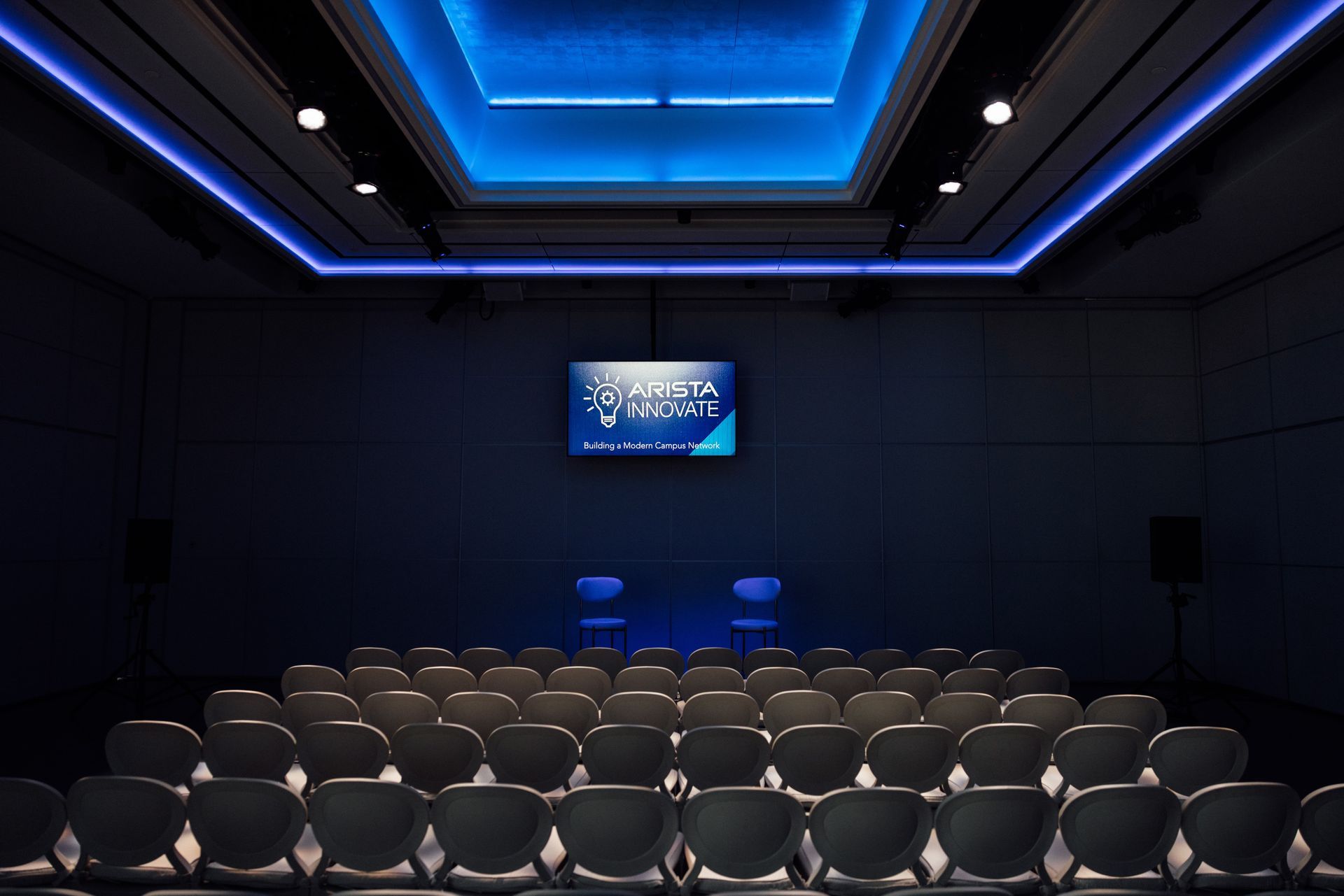 Auditorium with rows of seats facing a screen. Blue lighting illuminates the ceiling.