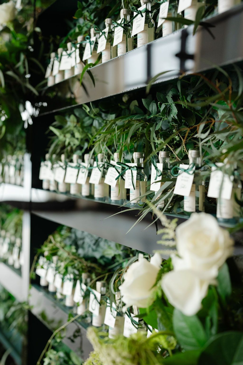 Shelves holding perfume bottles with tags, surrounded by greenery and white roses.