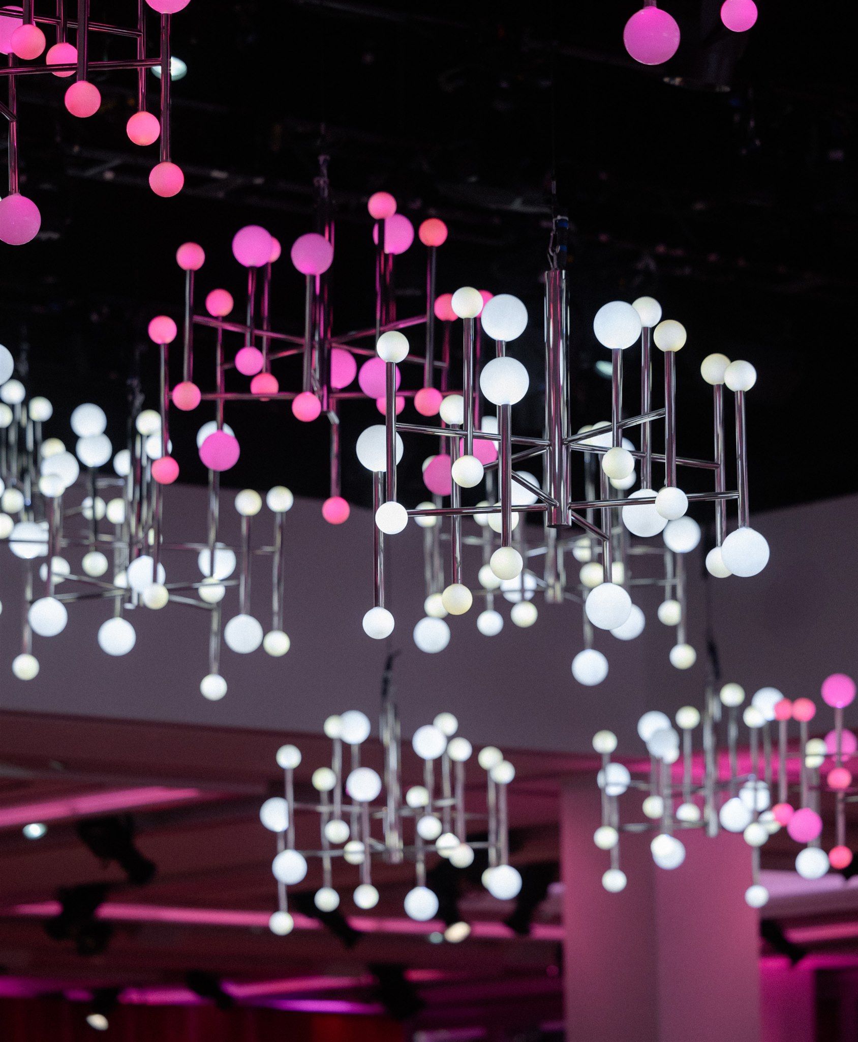 Pink and white globe lights hanging from a black ceiling, casting pink and white light on the setting.