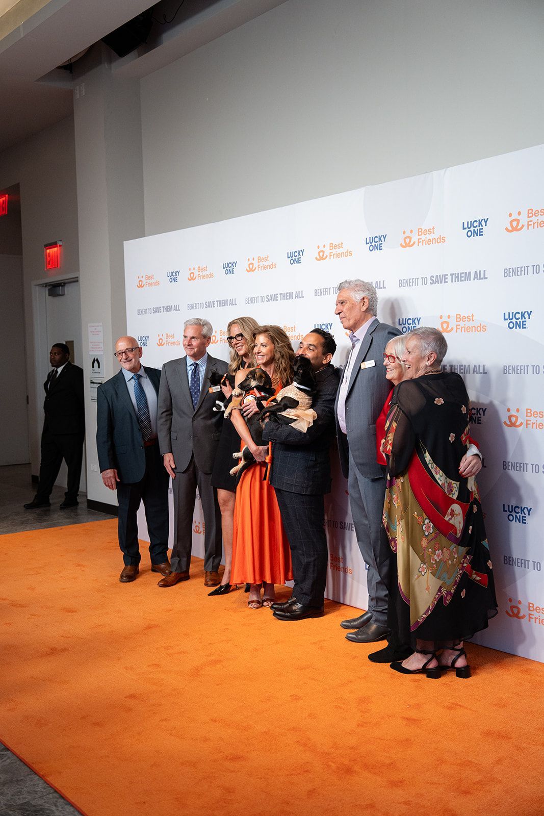 Group poses on orange carpet in front of a white backdrop with orange text.