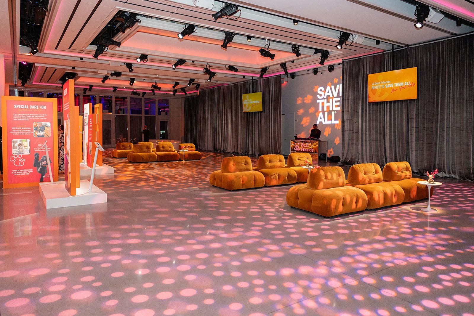 A room set for an event with orange seating, lighting, and signs; gray walls and floor.