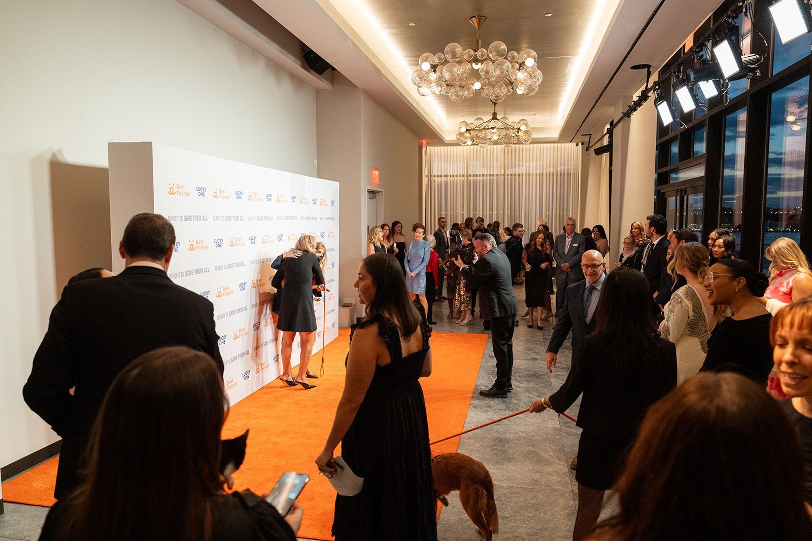 People at an event, many in formal attire, walk along a bright orange carpet.