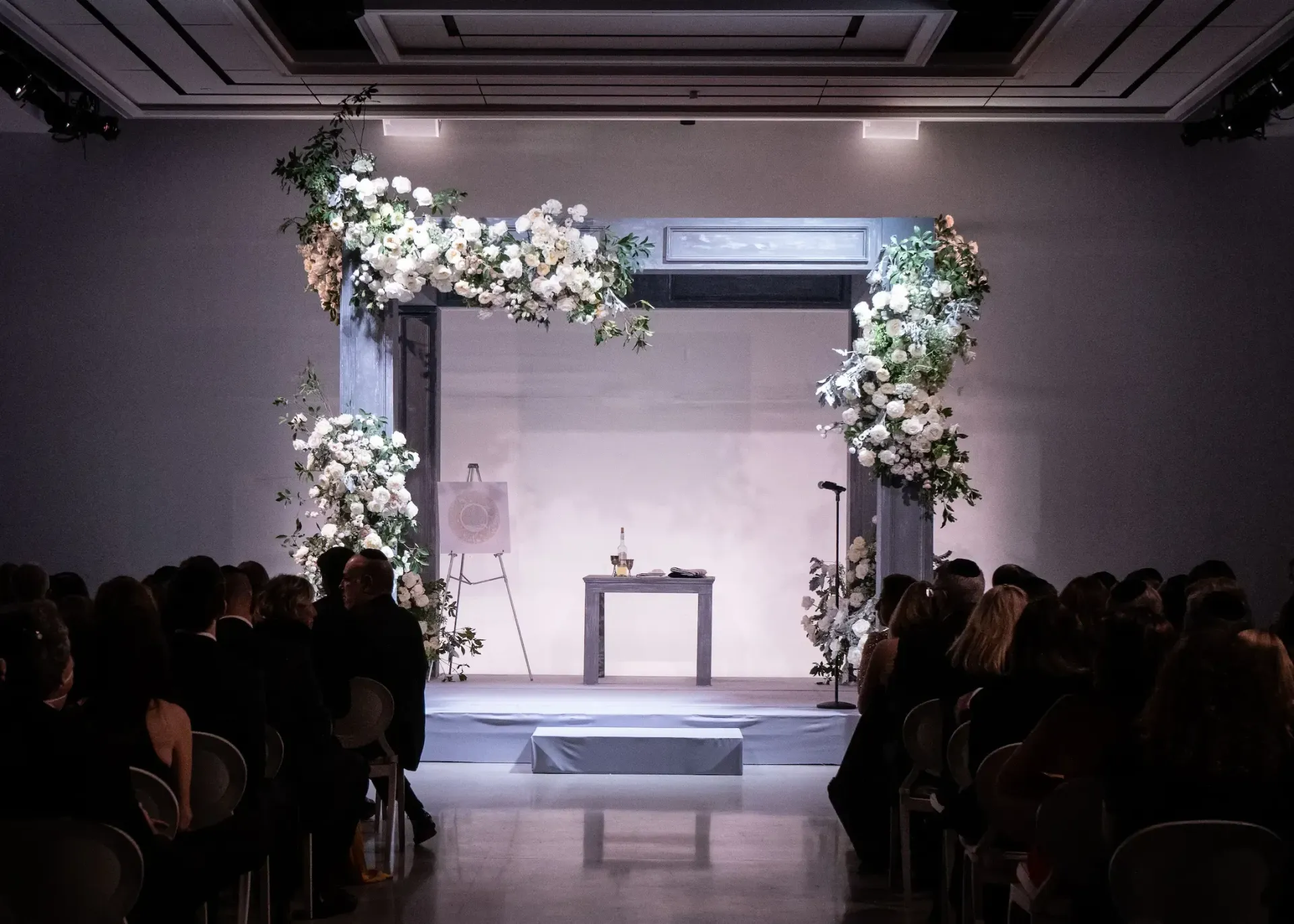A group of people are sitting in front of a stage decorated with flowers.