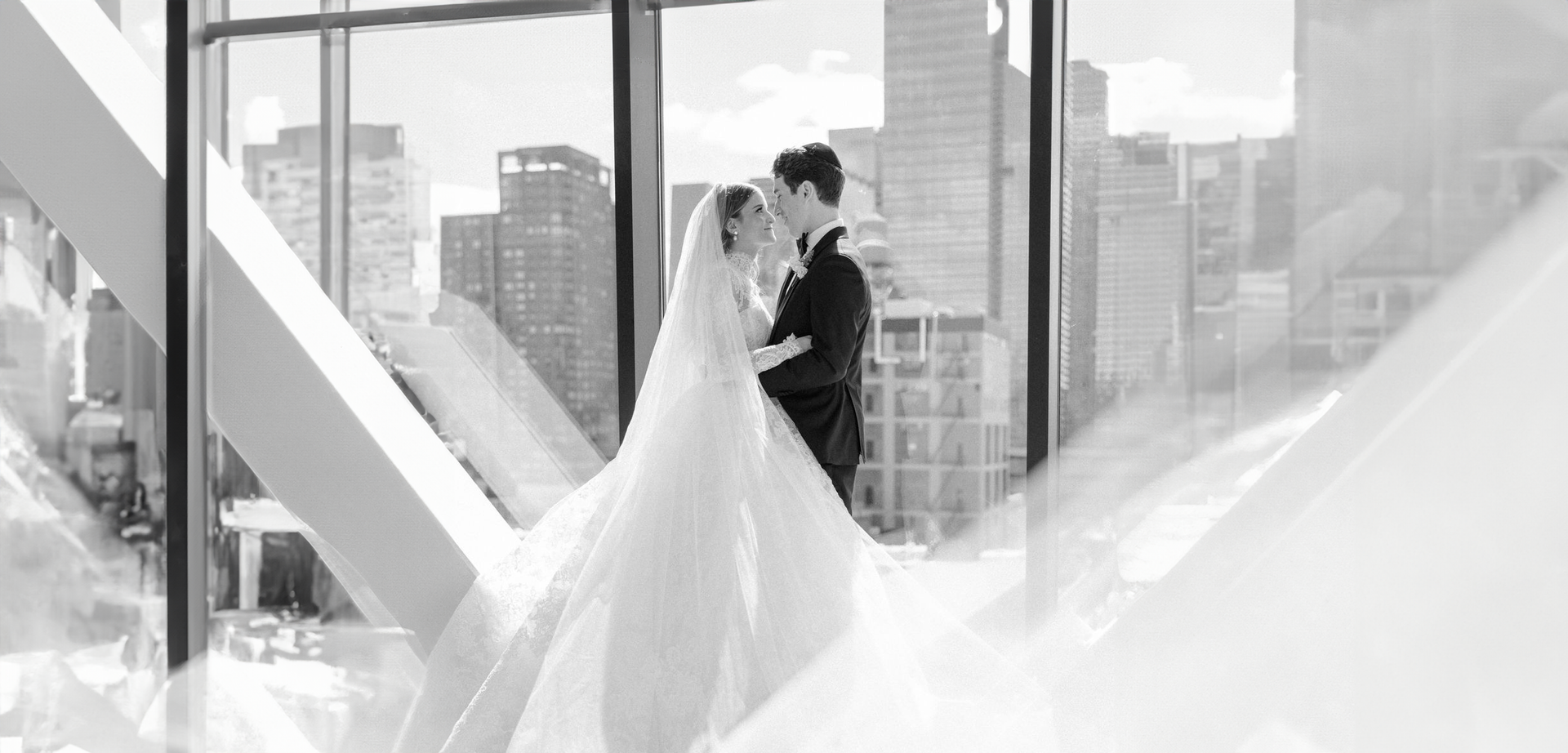 A bride and groom are kissing in front of a large window.
