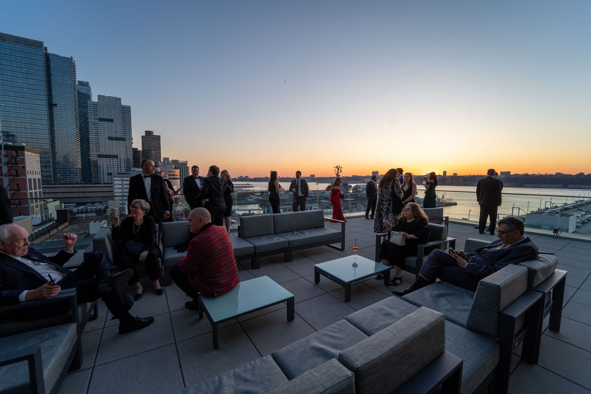 A group of people are sitting on a rooftop patio at sunset.