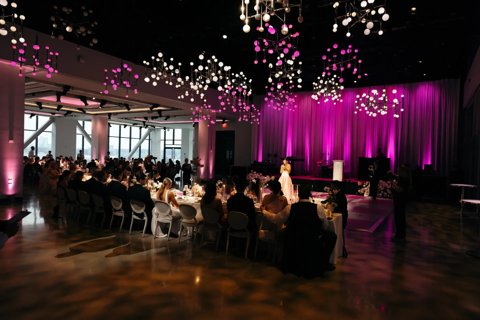 People are sitting at tables in a large room with purple lights on the ceiling