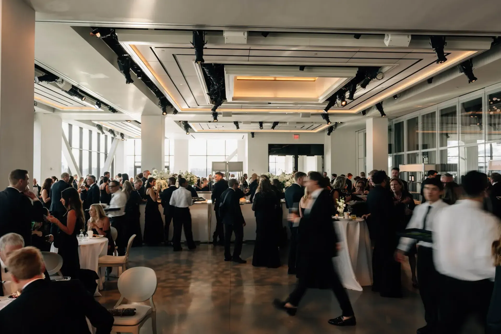 A large room filled with people standing around tables.
