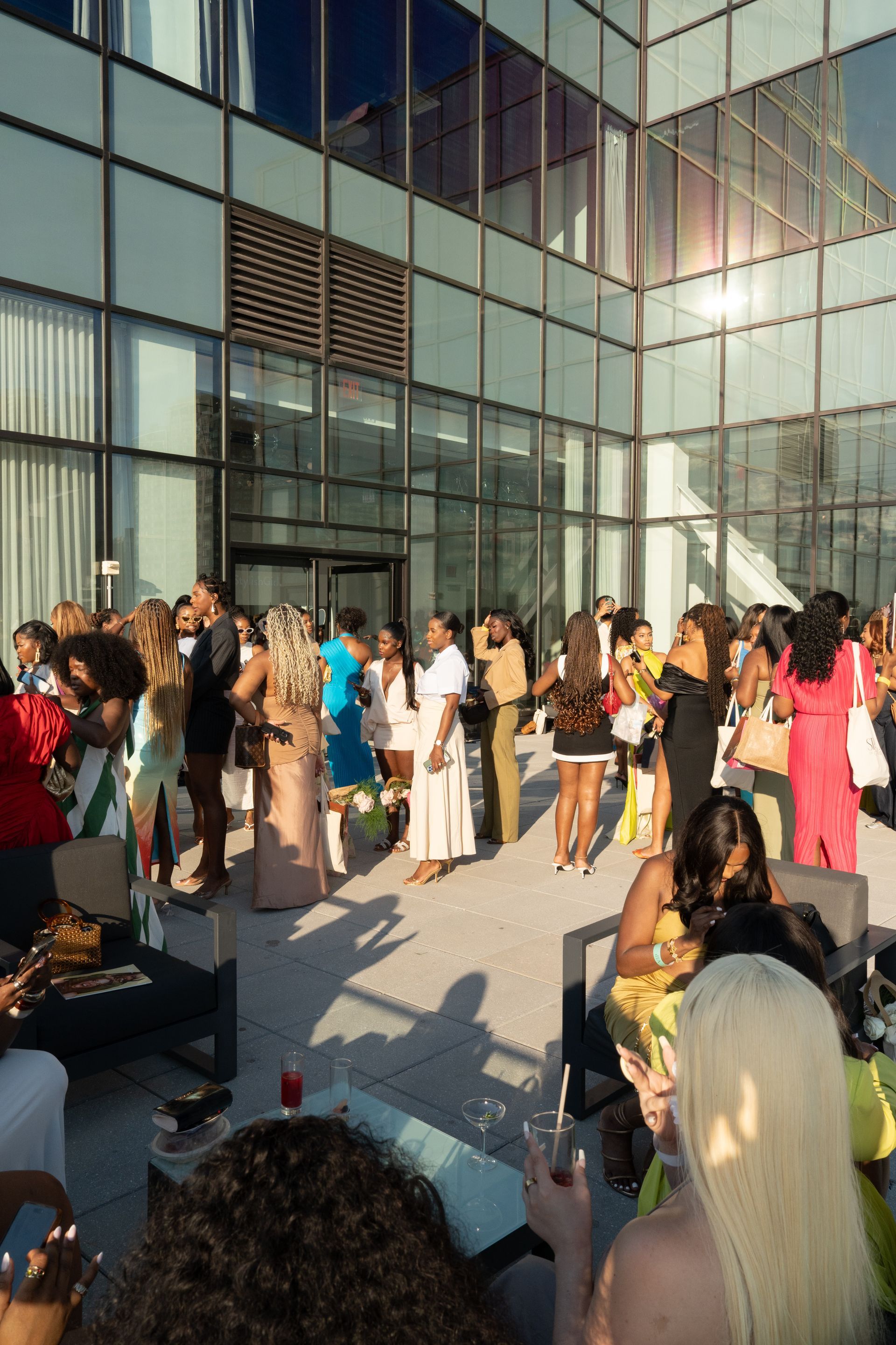 Outdoor event with diverse people socializing; sunlit patio, modern building.