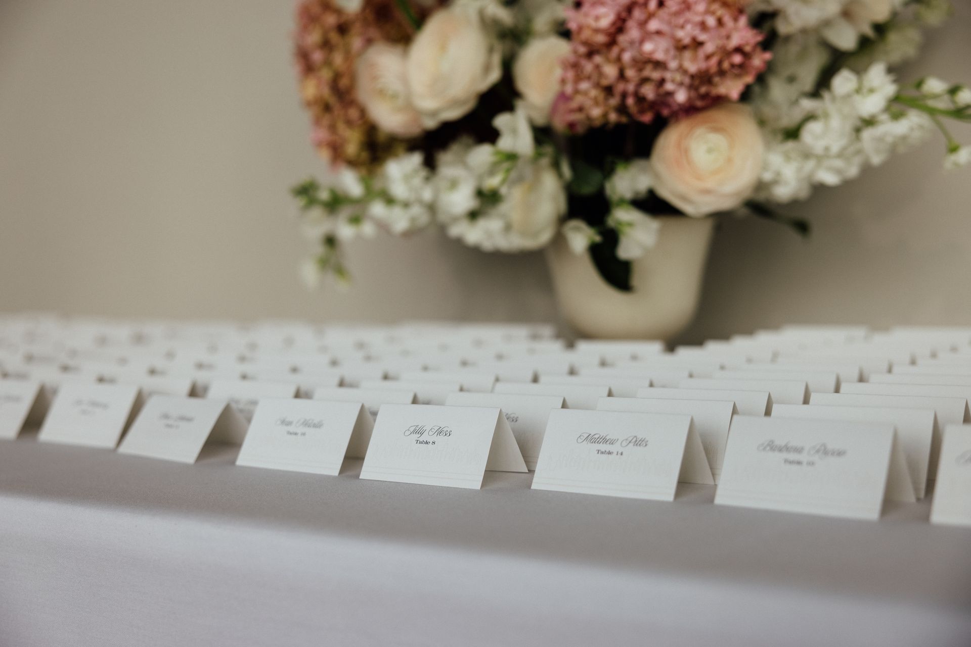 Place cards on a white table with a floral arrangement in the background.