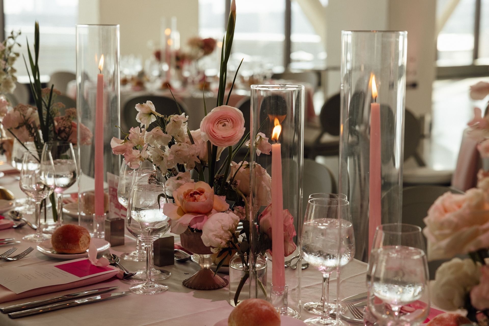 Elegant table setting with pink flowers, candles, and glassware.