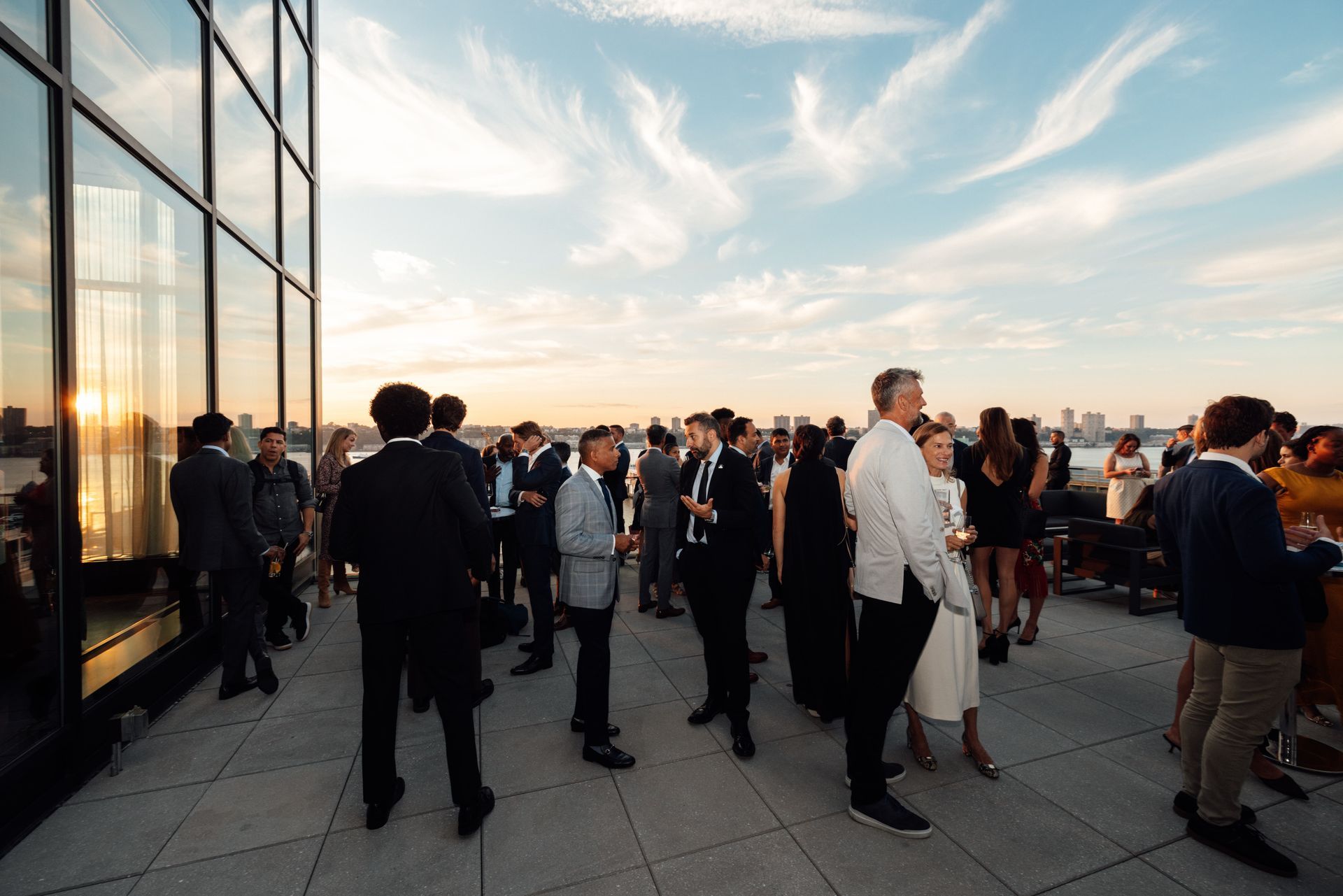 People gather on a rooftop patio with a cityscape background and cloudy sky.