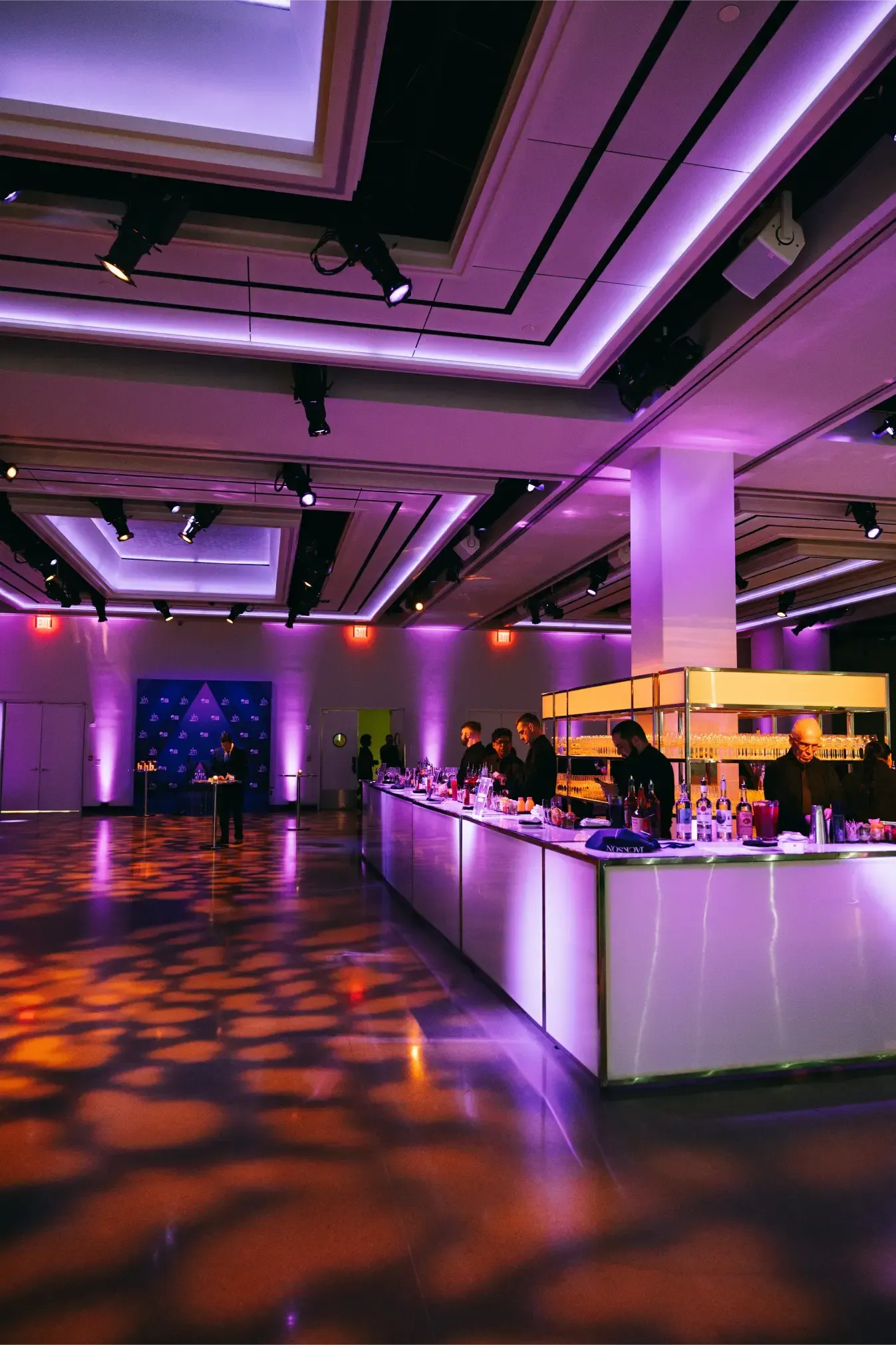 A large room with purple lights on the ceiling and tables.