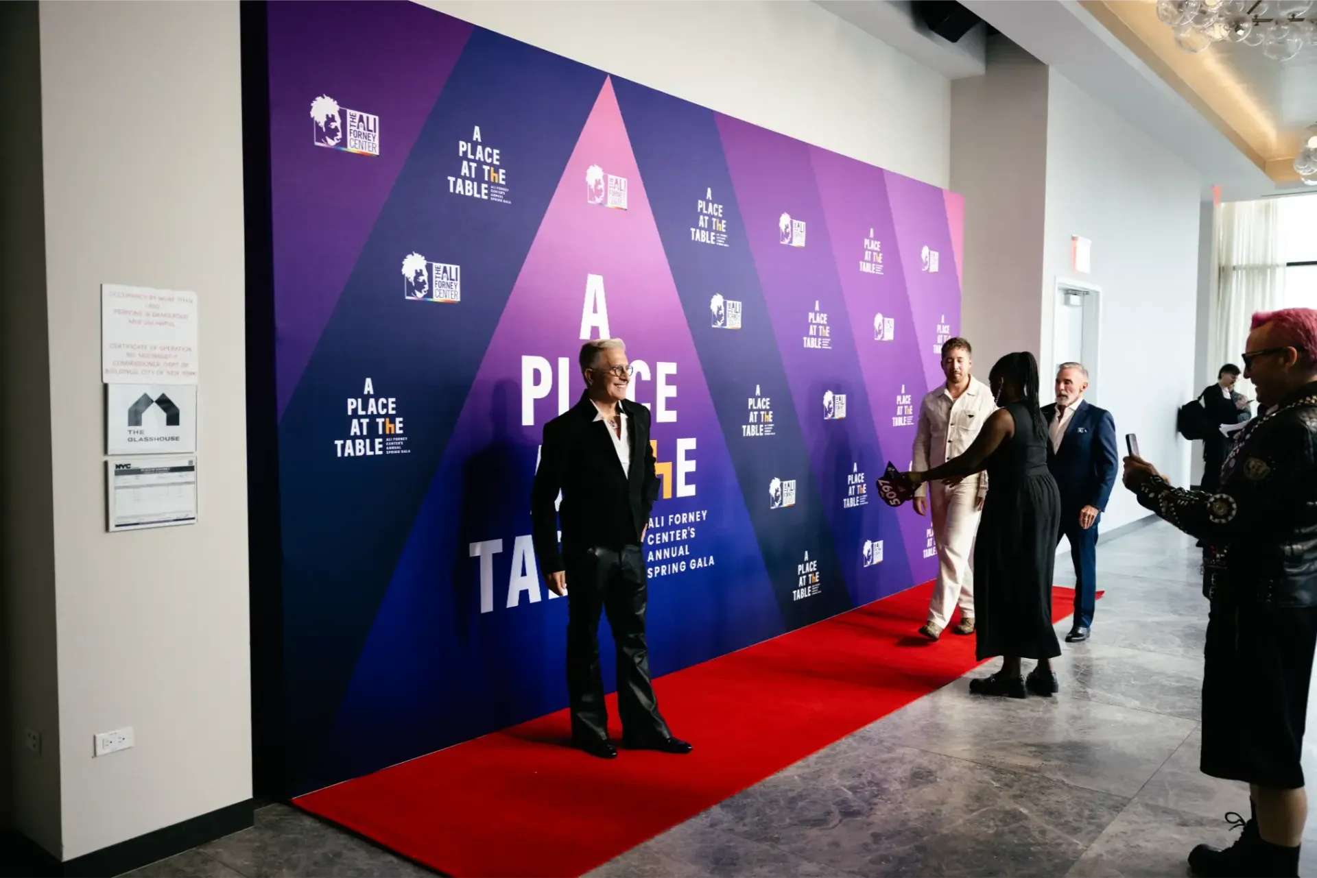A group of people are standing on a red carpet in front of a wall.