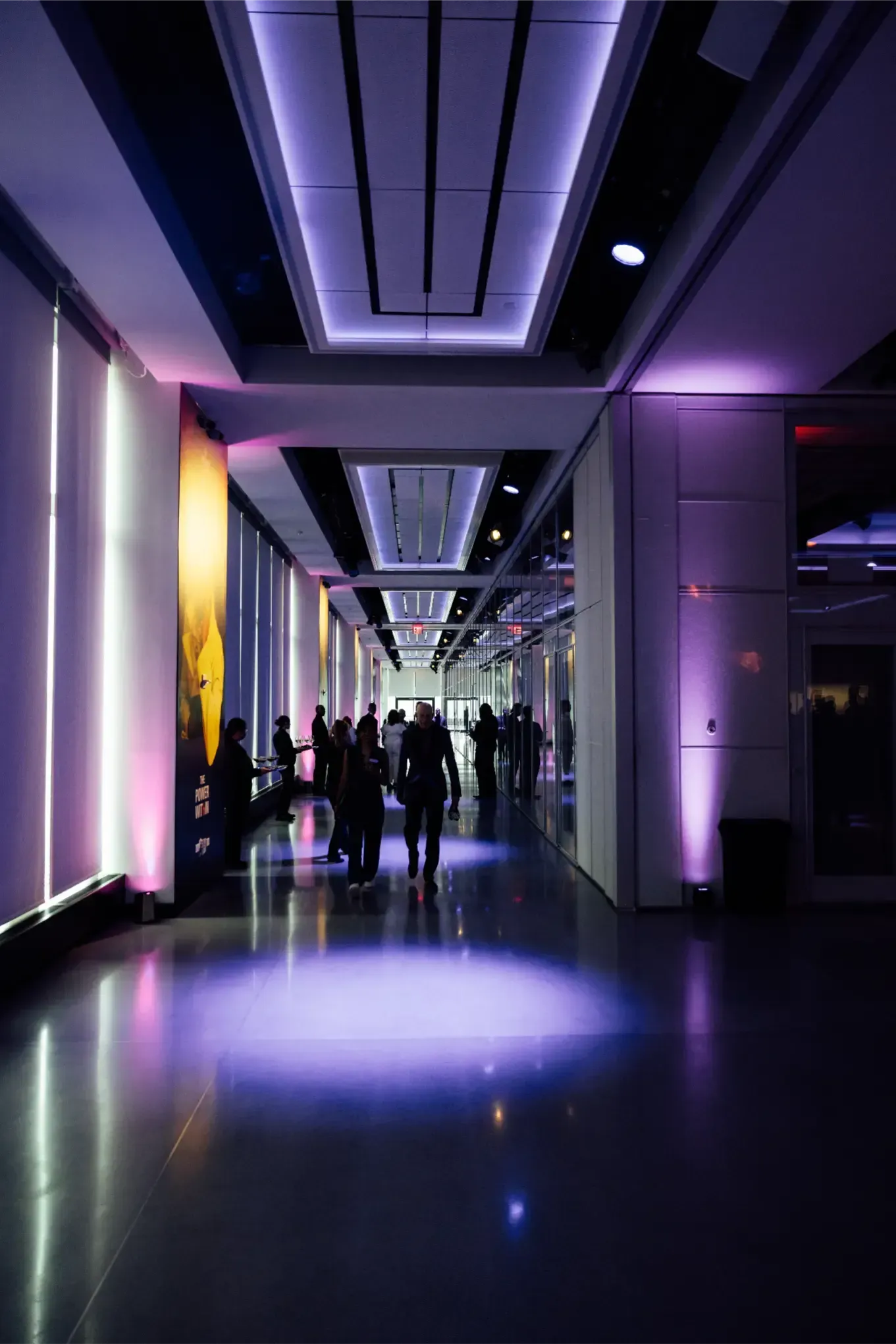 A group of people are walking down a hallway with purple lights.