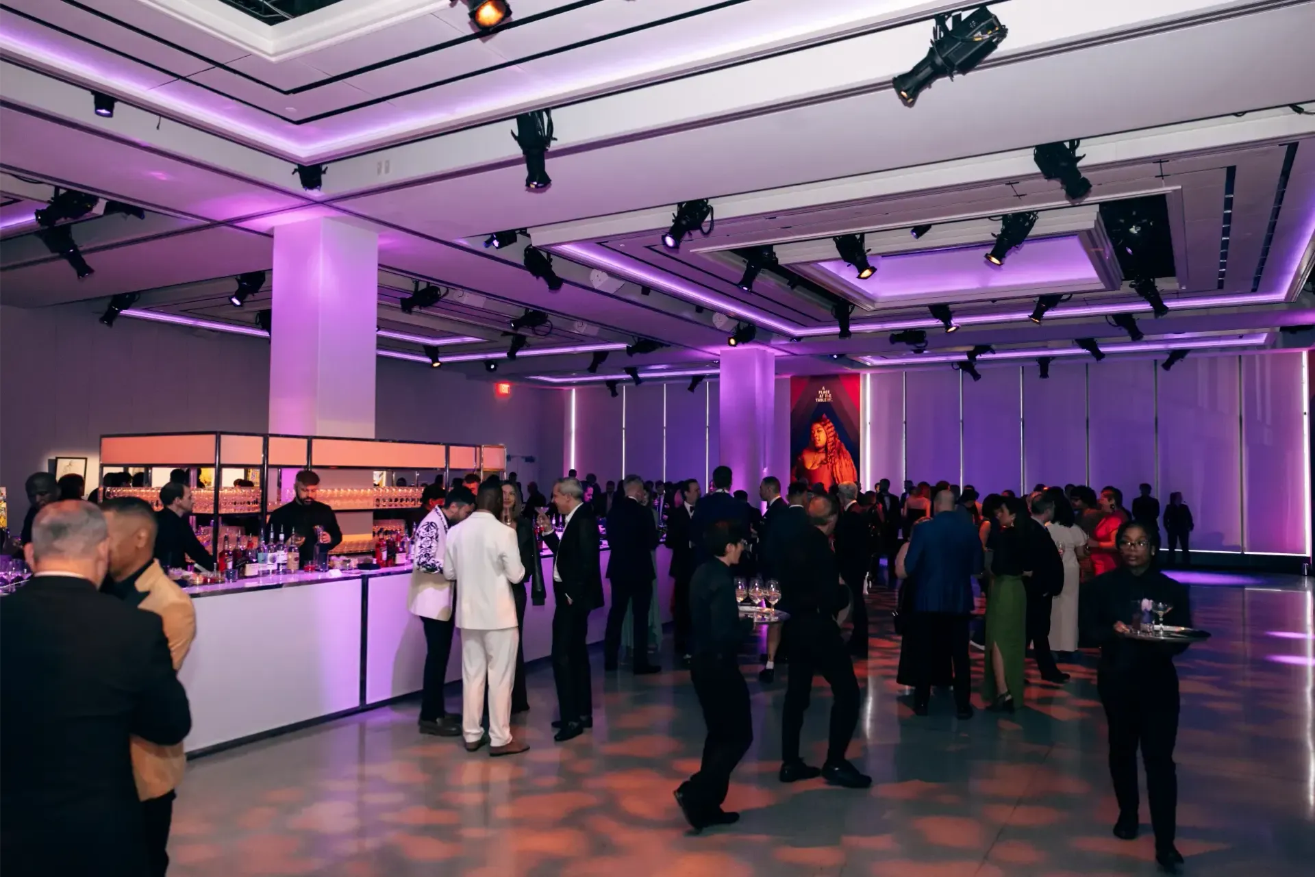 A group of people are standing in a large room with purple lights.