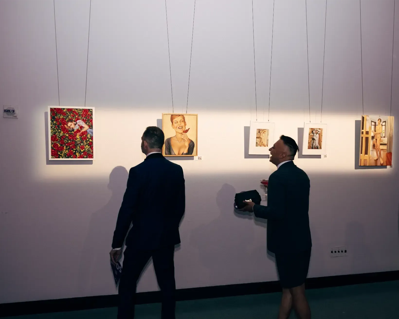 Two men are looking at paintings on a wall in a museum.