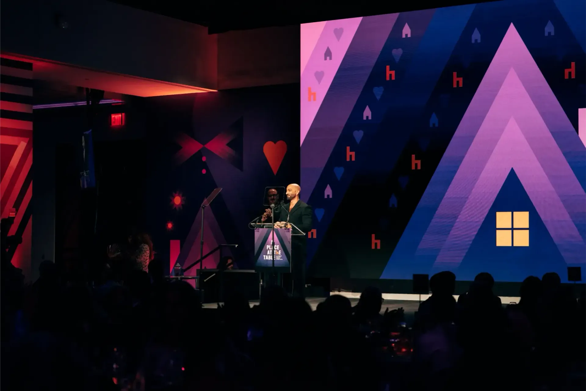 A man is standing at a podium giving a speech in front of a large screen.