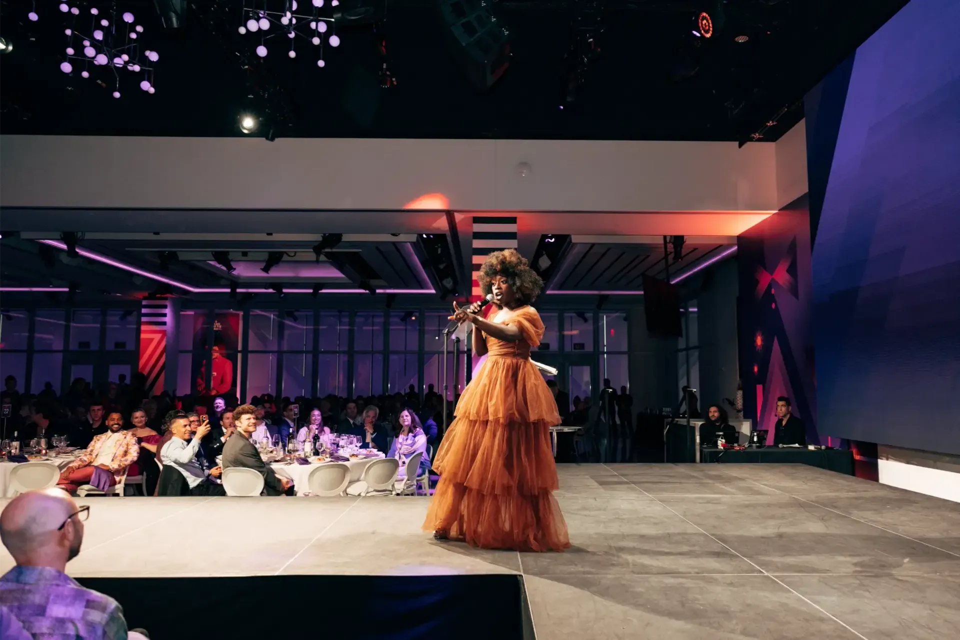 A woman is standing on a stage singing into a microphone.