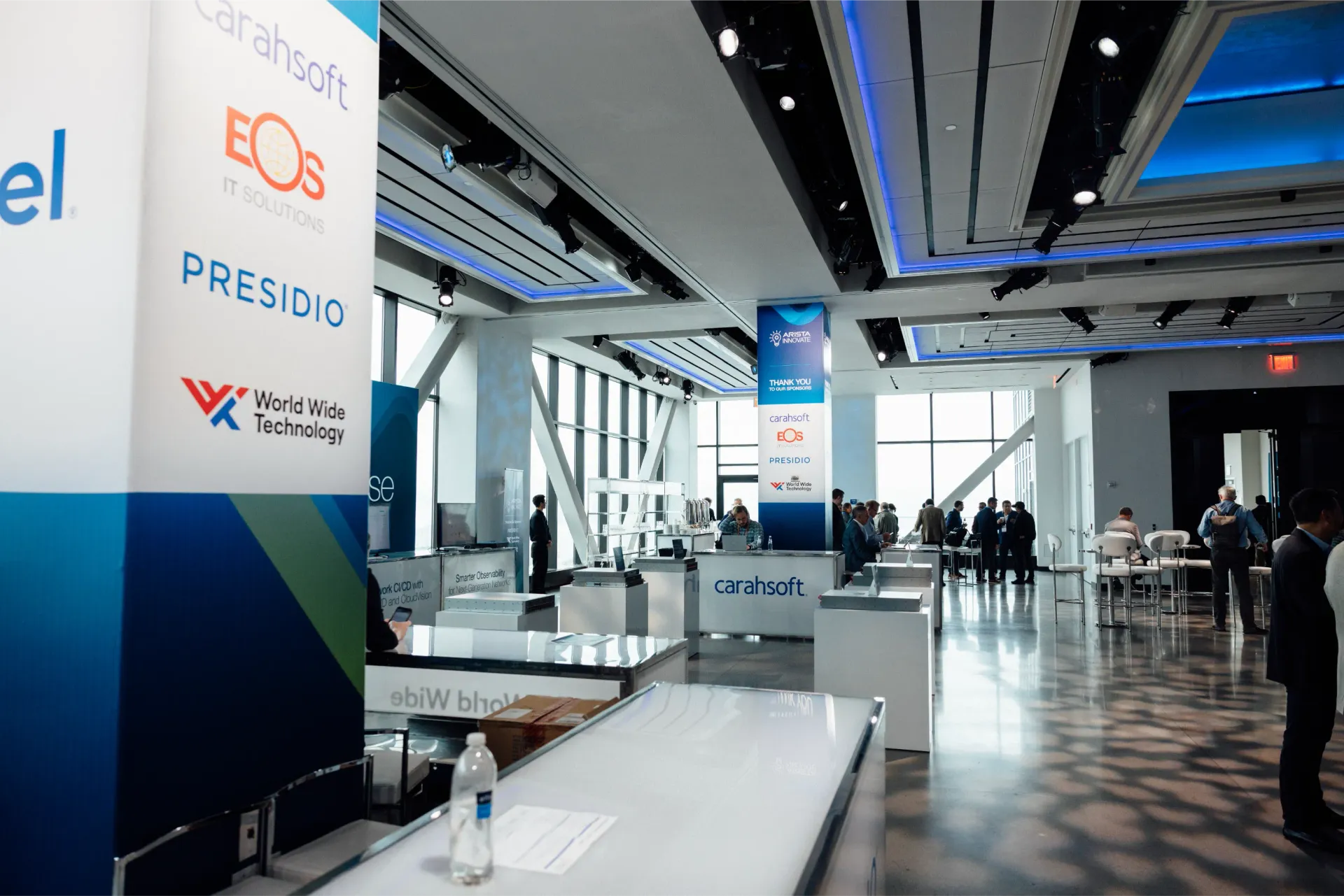 Conference room with signs, tables, and people; blue, white, and glass accents.