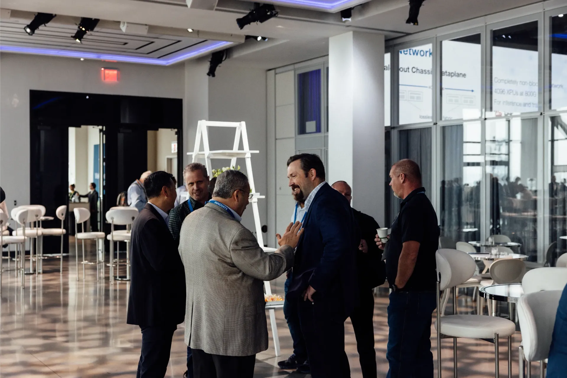 Group of men in suits and casual wear conversing in a bright, modern conference room.