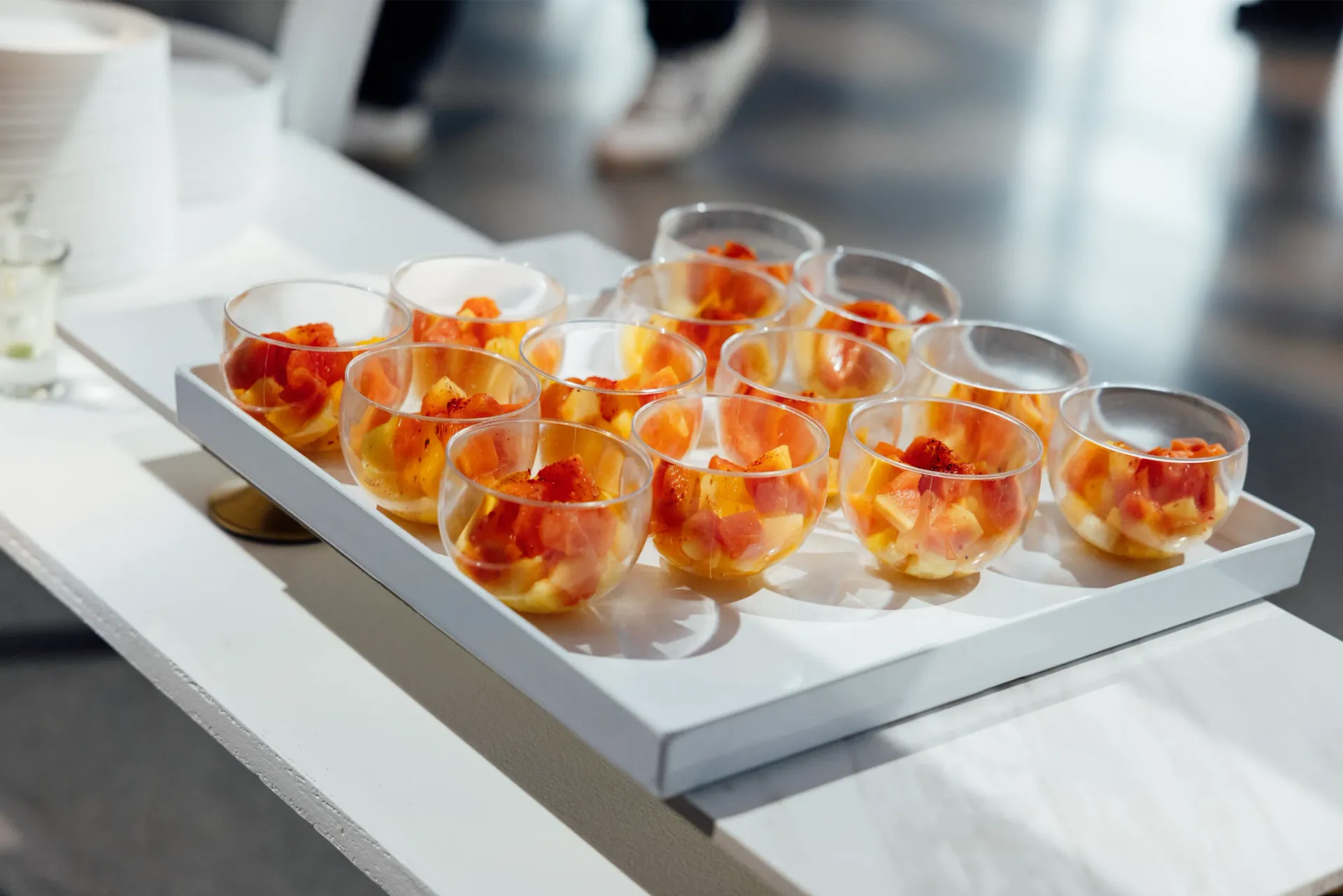 A tray of clear glasses filled with orange fruit on a white table.