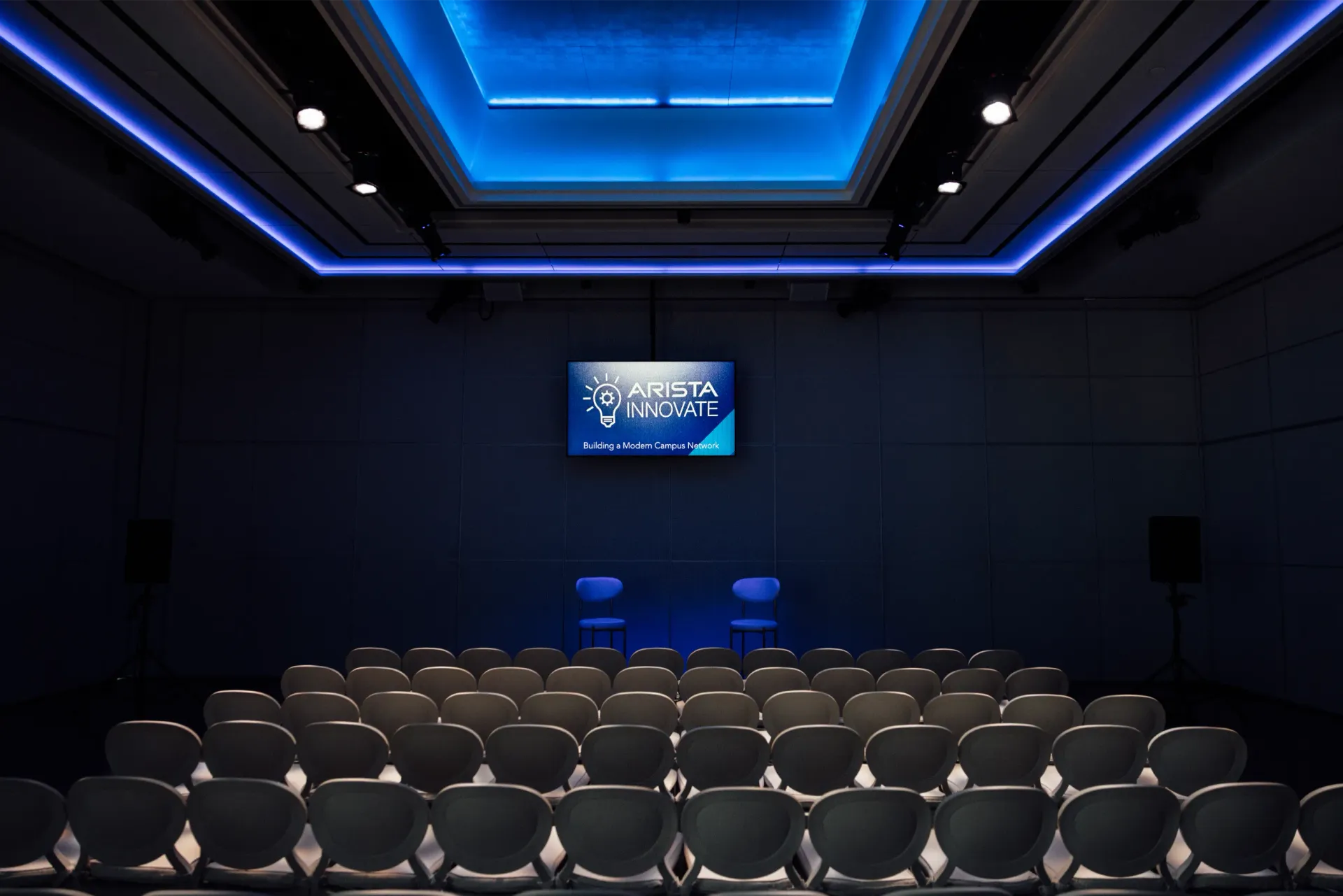 Audience seating in a dark room facing a screen. Blue lights illuminate the ceiling.