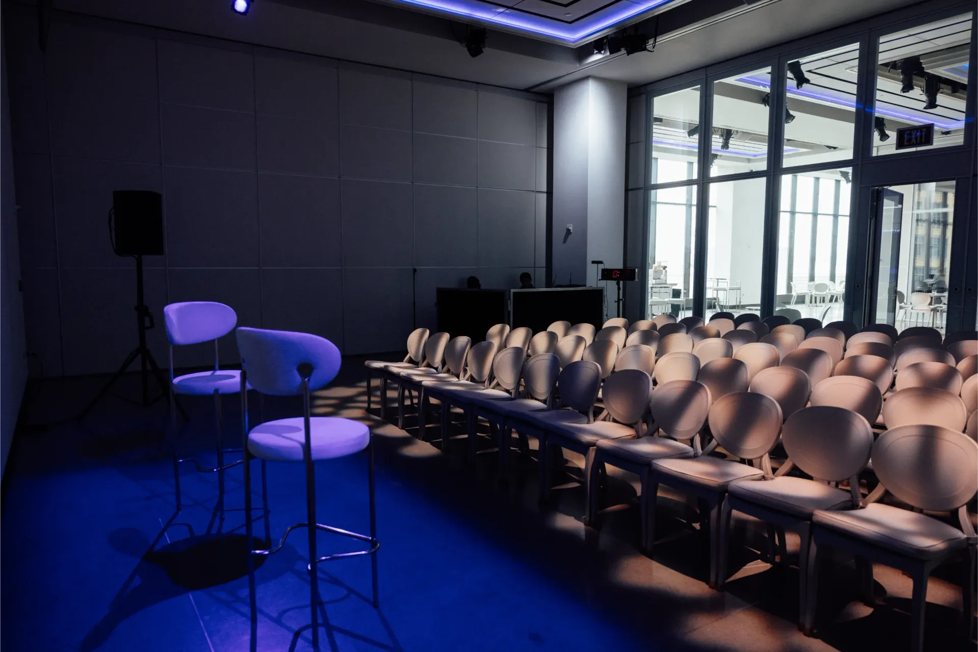 Empty auditorium with rows of chairs and a podium, illuminated by blue lighting.