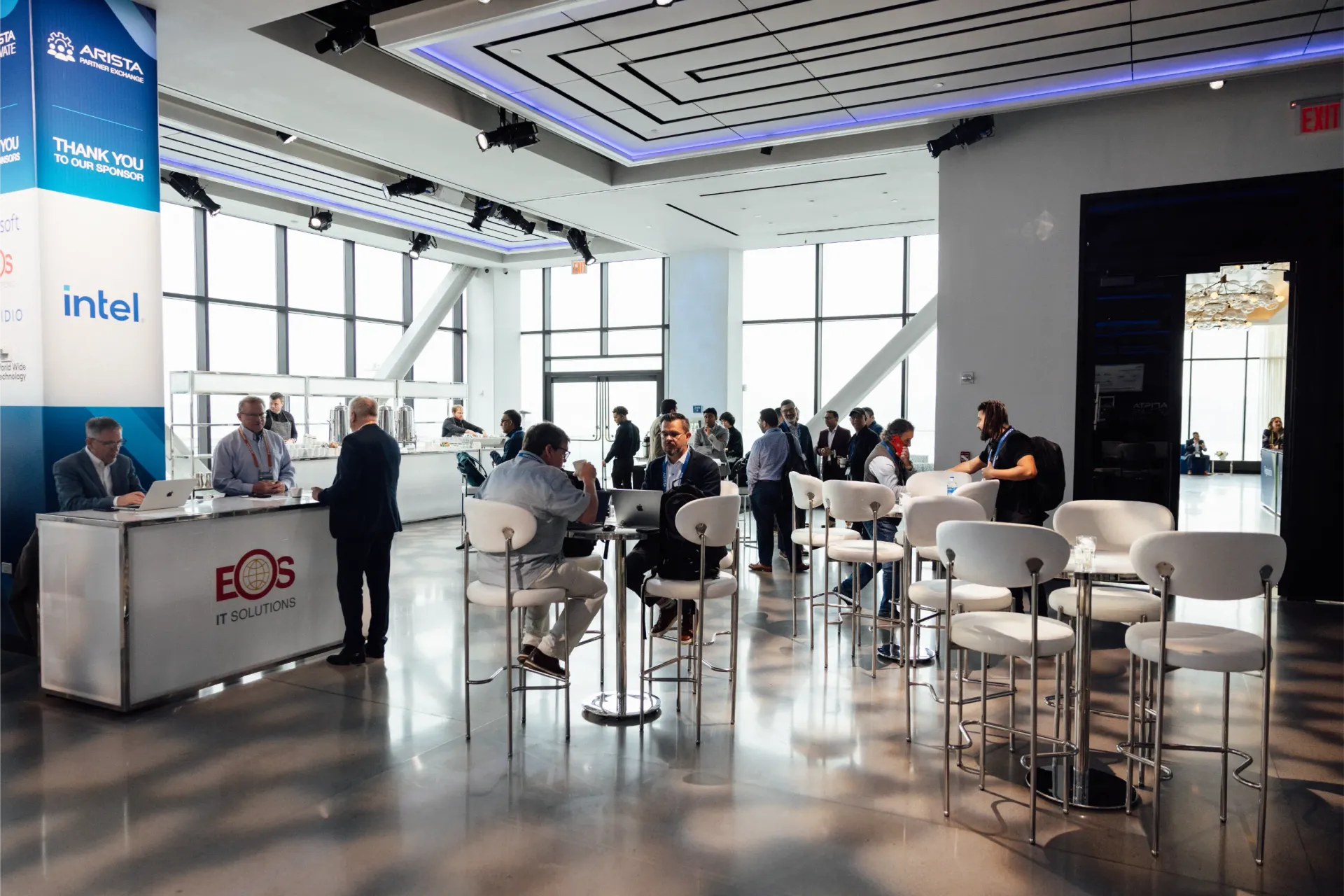 Event venue with people mingling. A booth, high-top tables and bar stools. Blue accents, bright light.