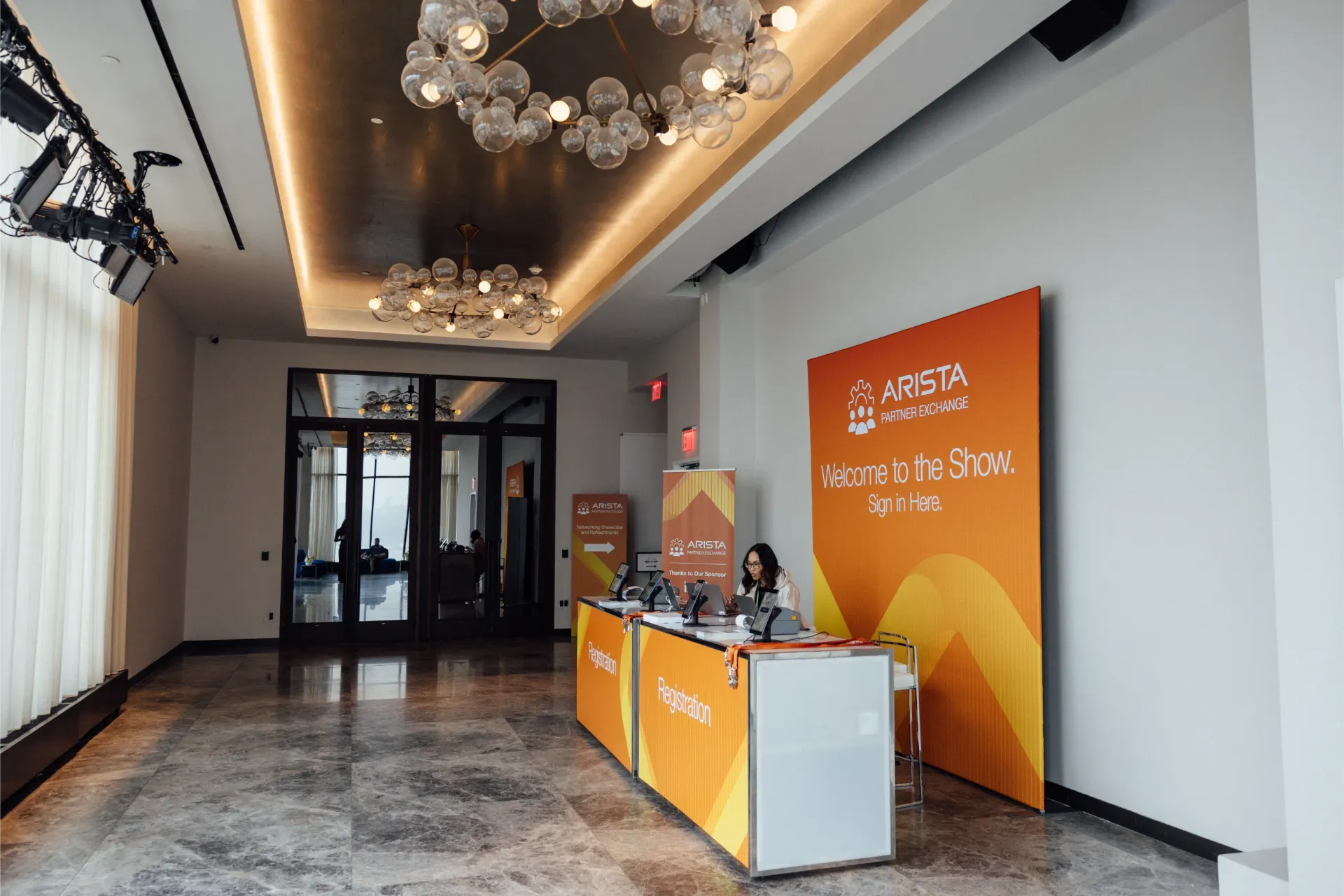 A hallway with a registration desk for an event. Orange and white signage; person seated.