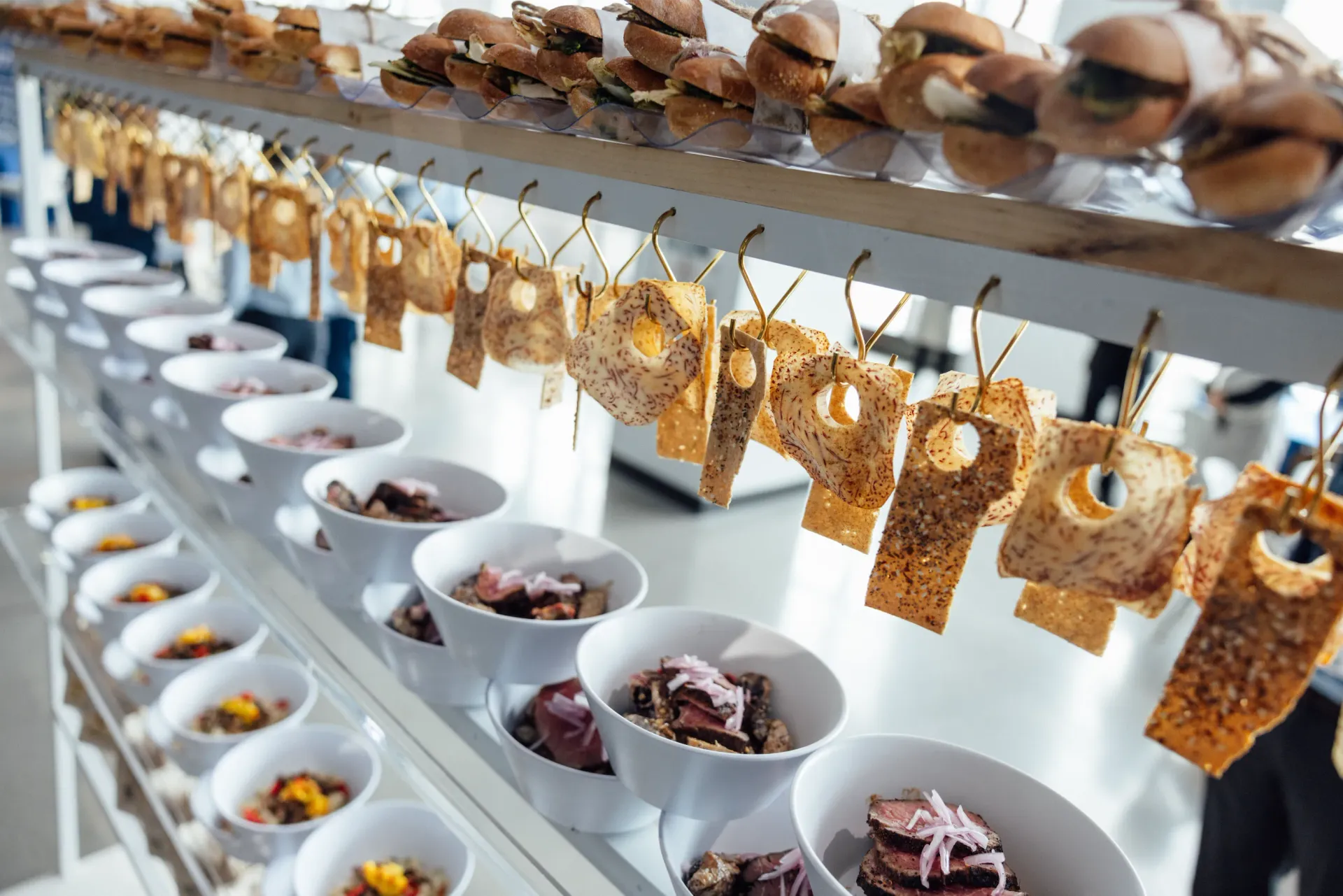 Appetizers arranged on shelves. Small burgers, bowls of food, and tagged crackers.