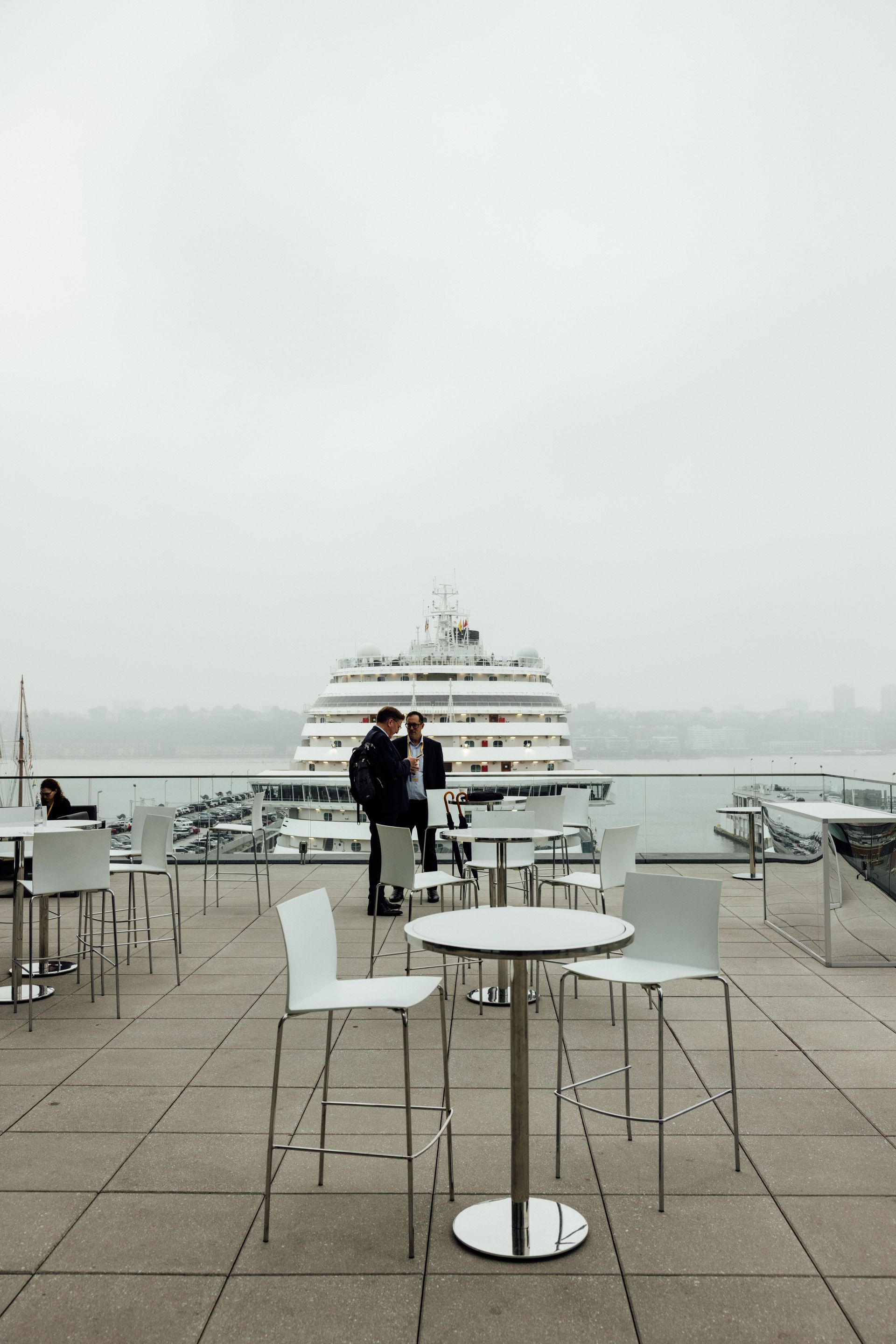Outdoor cafe overlooking a large ship on a foggy day. Two figures stand near the railing.
