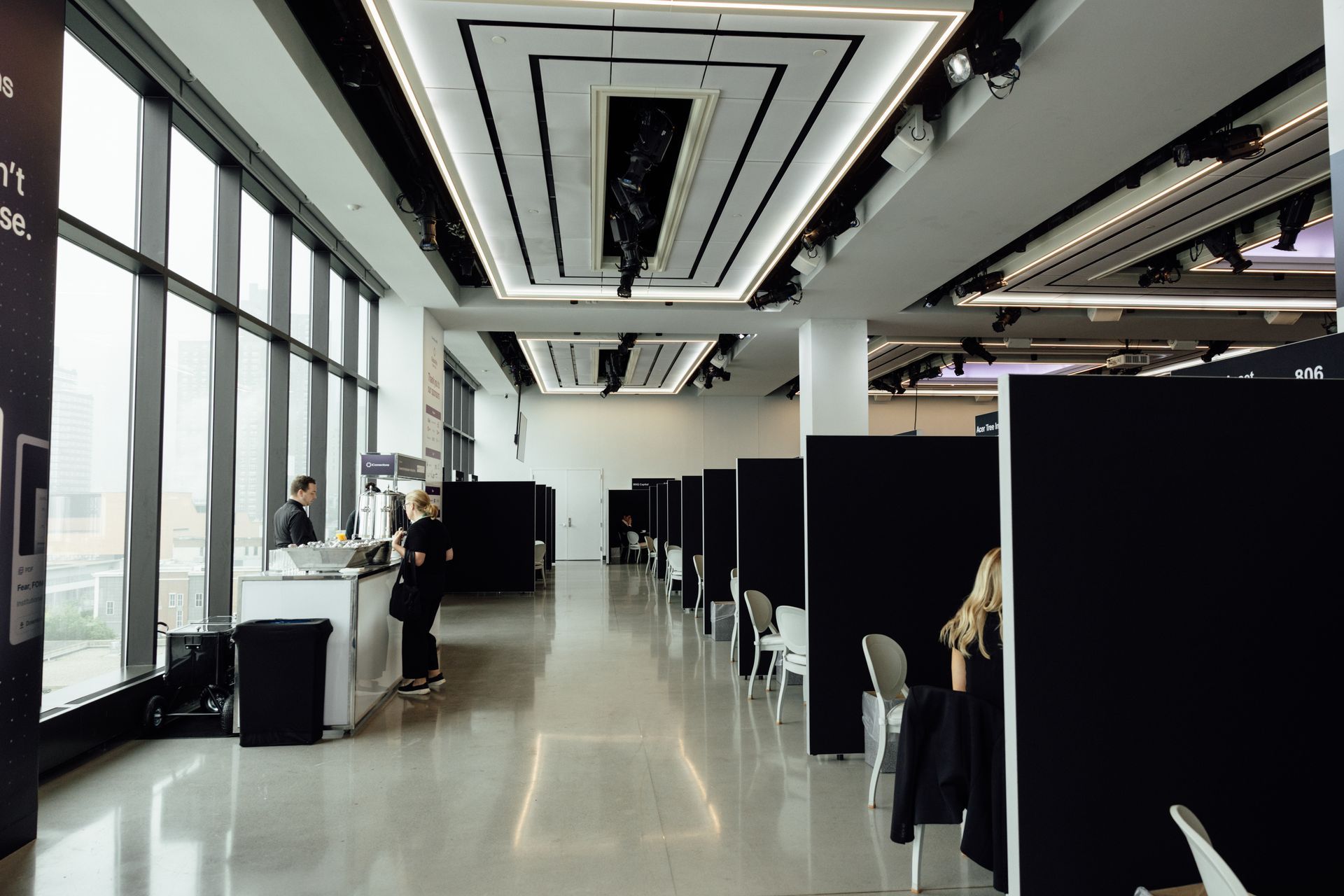 Spacious, modern interior with floor-to-ceiling windows. Black dividers create individual spaces. People stand near a counter.