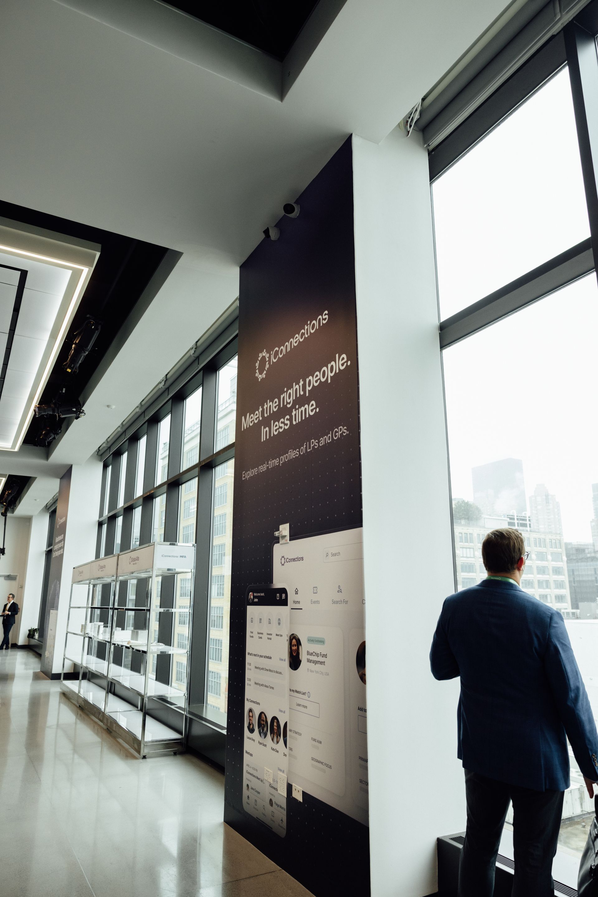 Man in suit looks out large windows. Building interior. Dark blue advertisement on pillar.