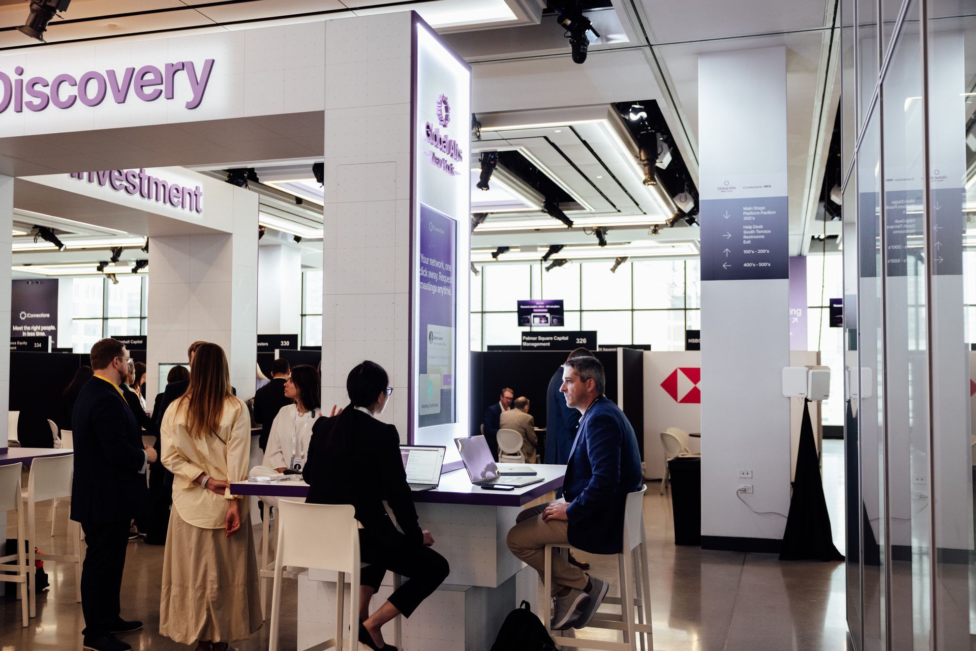 People at a Discovery investment booth. White and purple signage. Business attire. Well-lit office space.