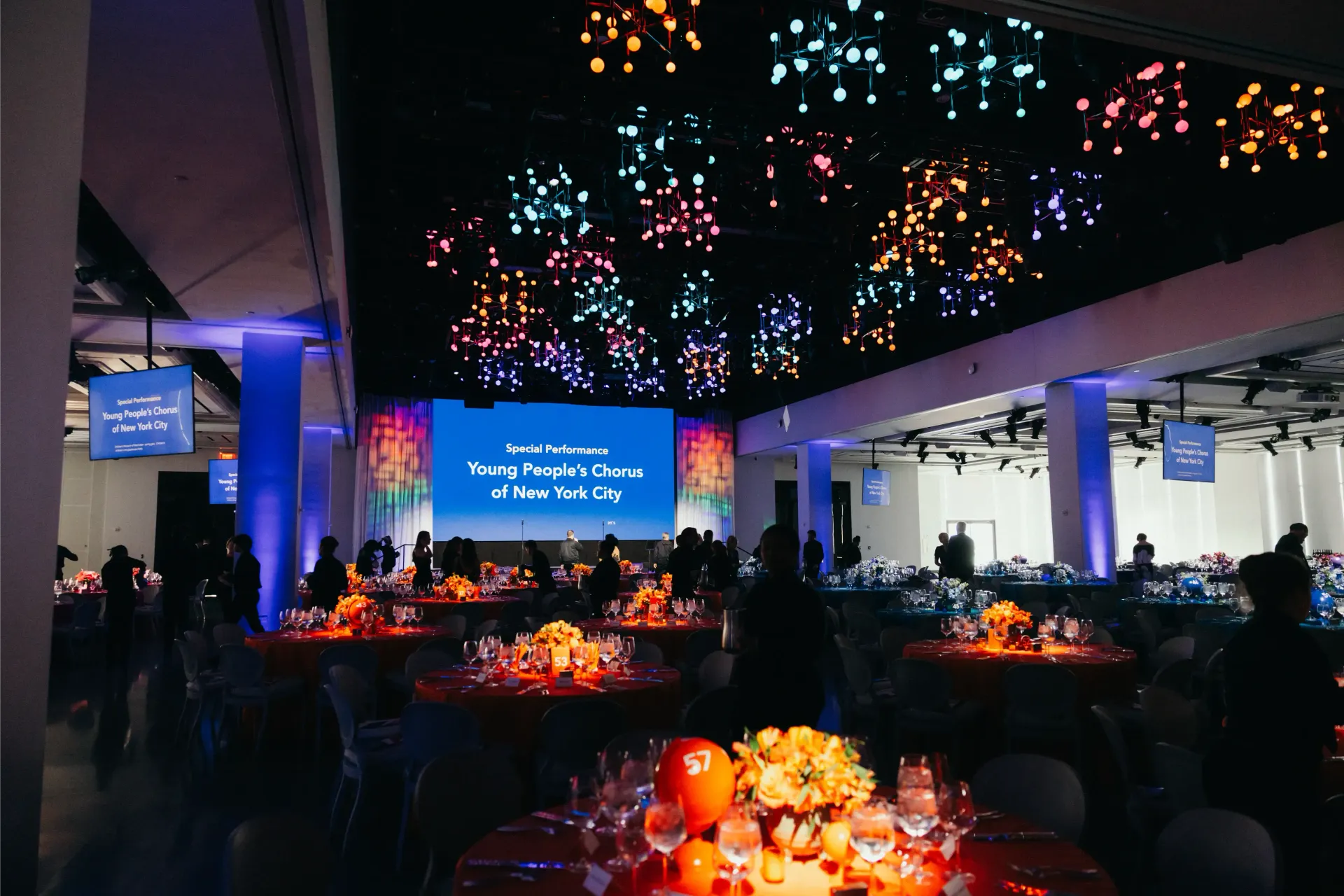 A large room with tables and chairs and a large screen on the ceiling.