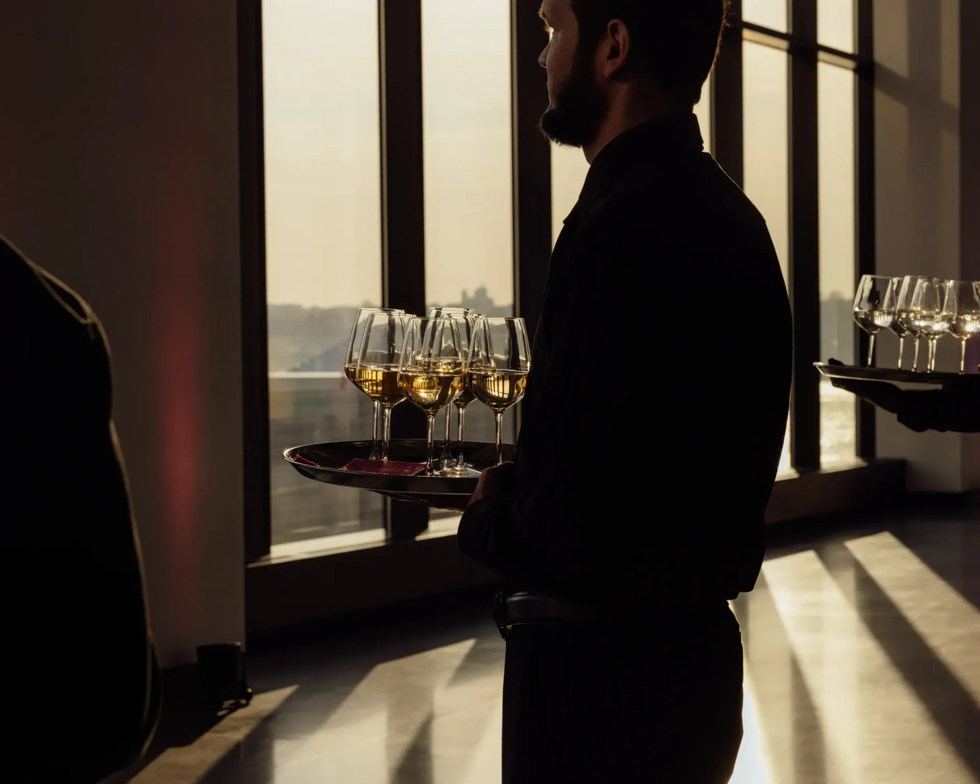 A man in a black shirt is holding a tray of wine glasses.