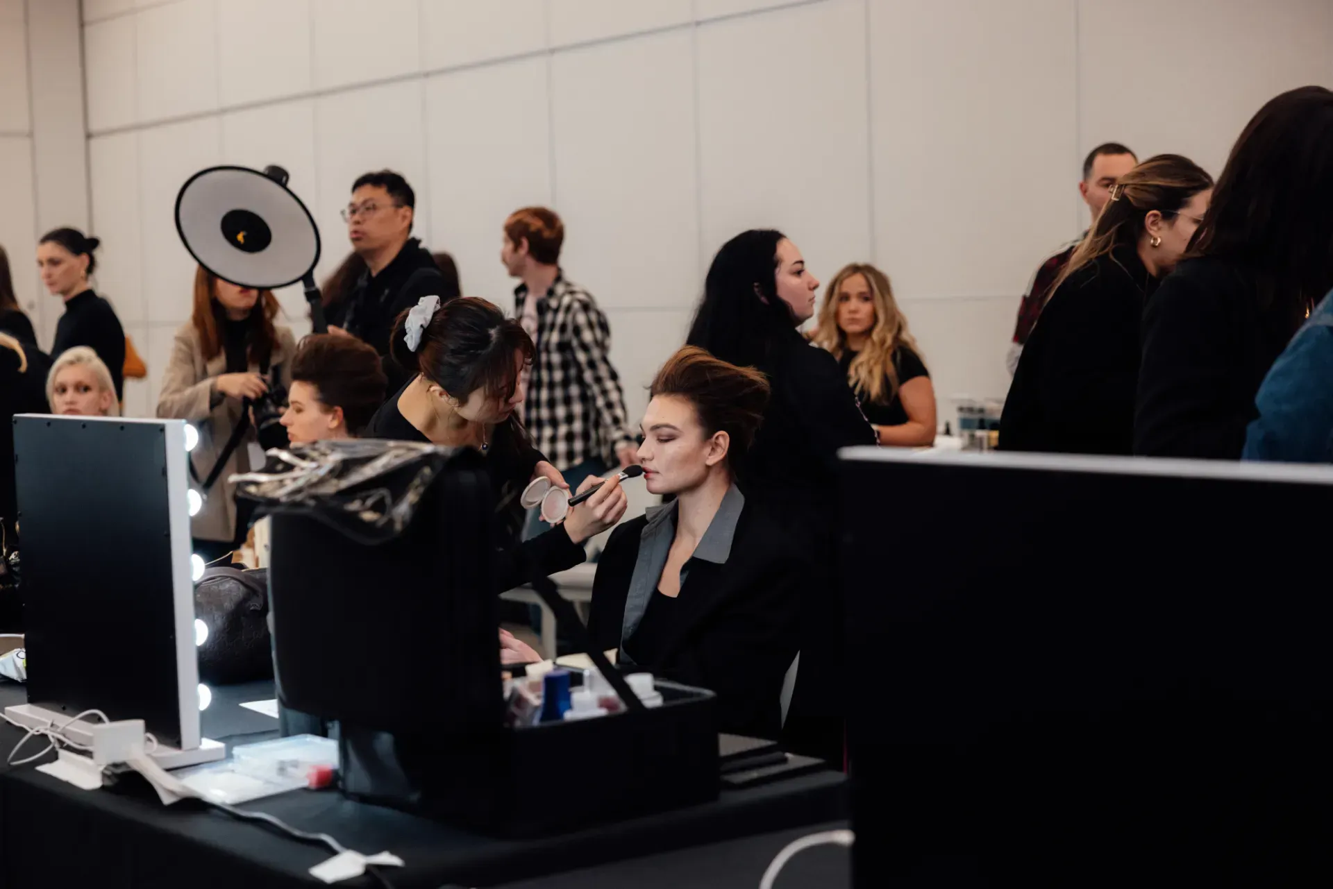 A woman is getting her makeup done in a room with a lot of people.
