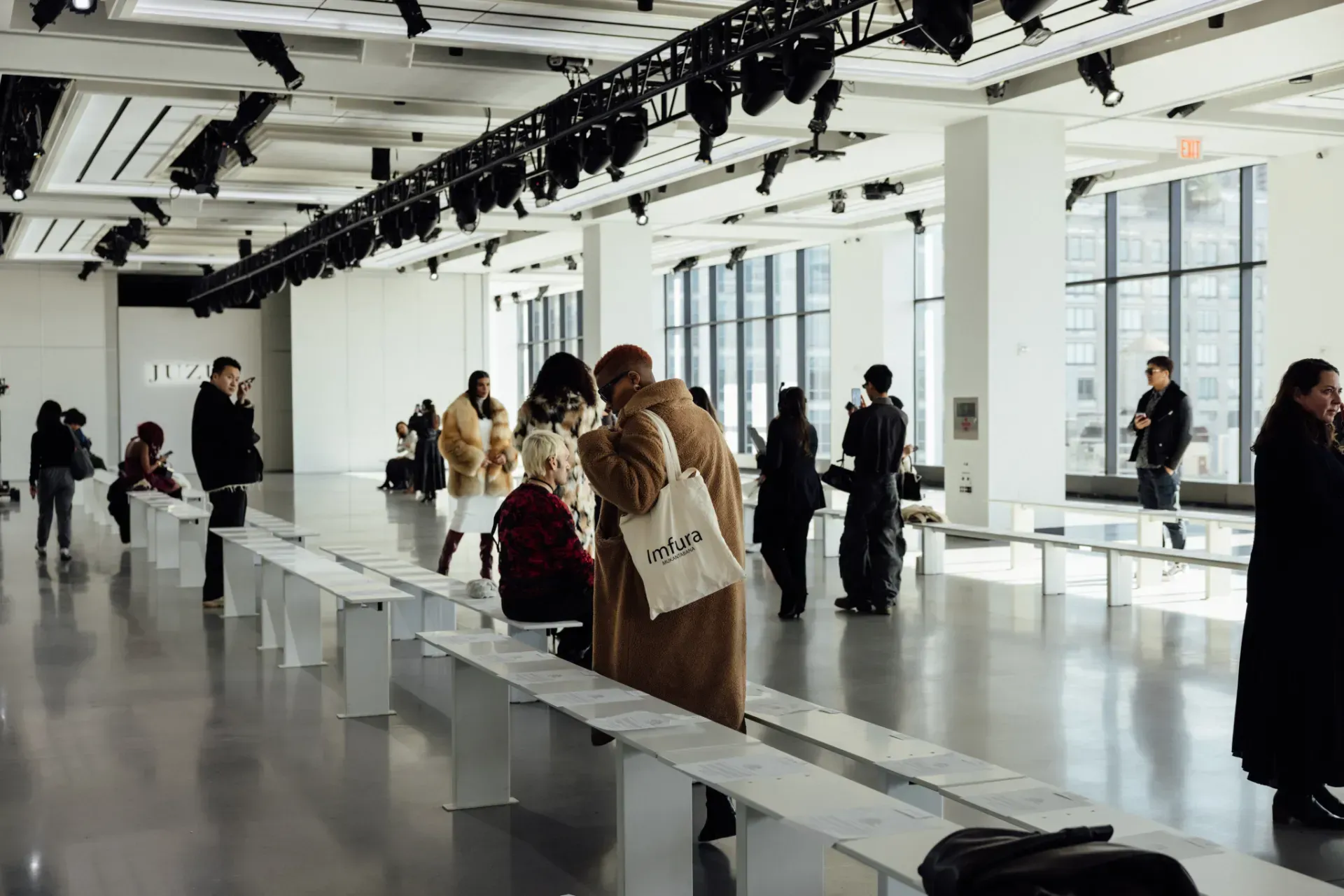 A group of people are standing in a large room at a fashion show.