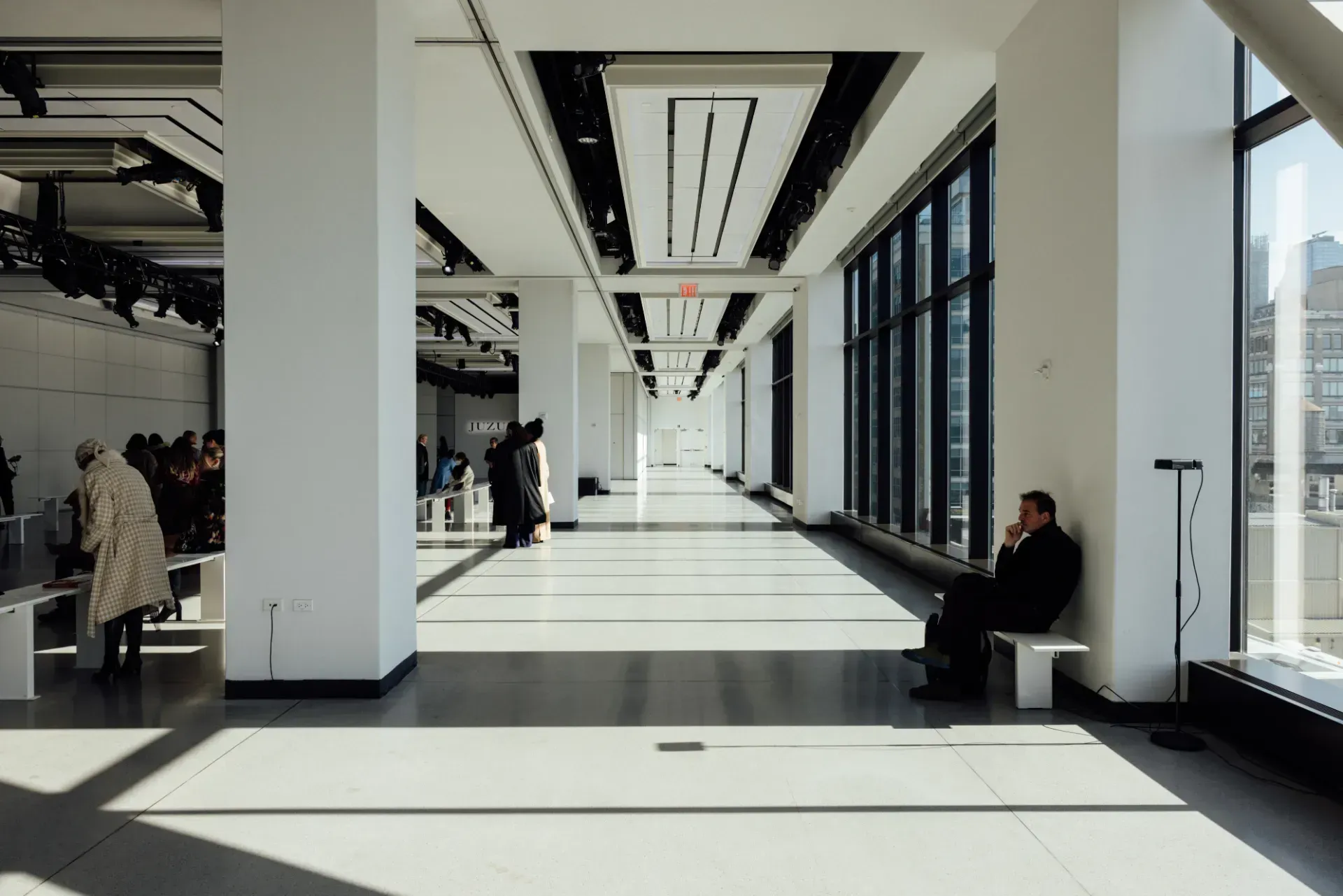 A man is sitting on a bench in a long hallway.