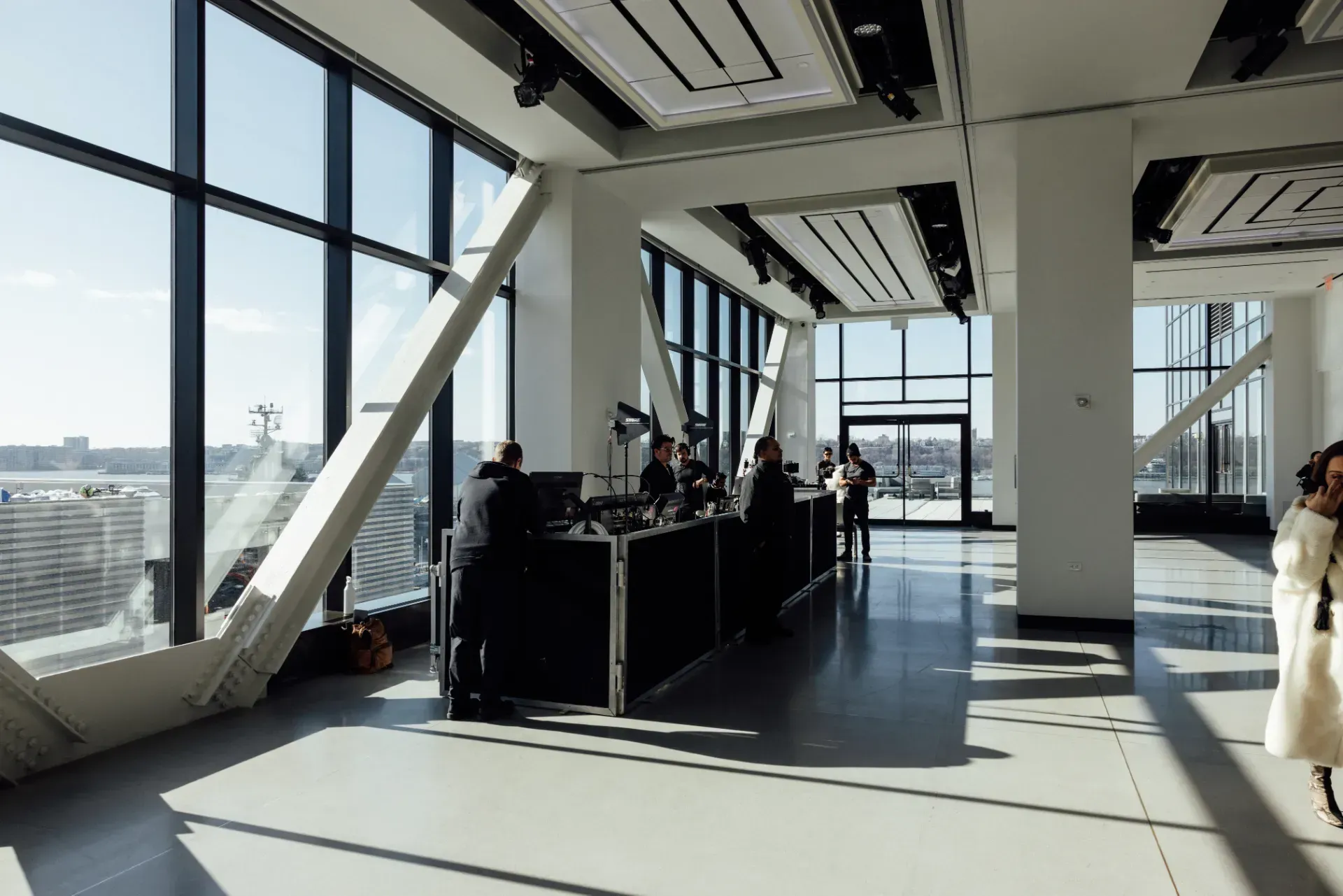 A woman is walking through a large room with a lot of windows.