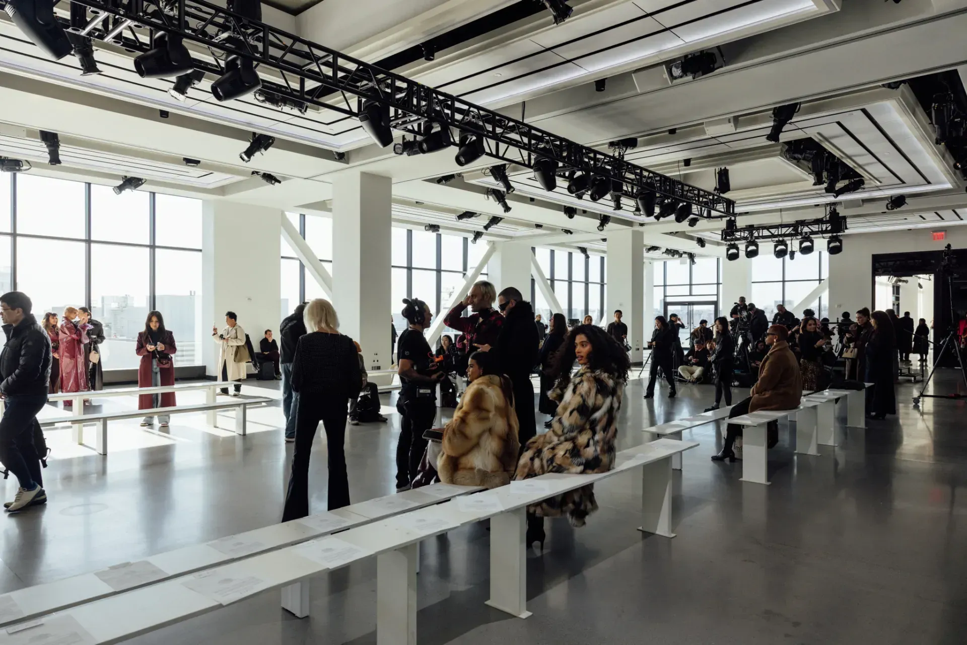 A group of people are standing and sitting in a large room at a fashion show.
