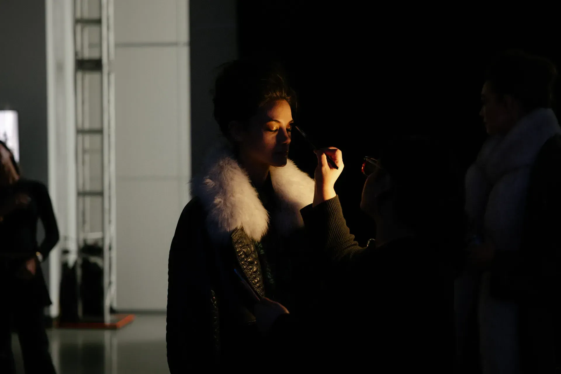 A woman is getting her makeup done by a makeup artist in a dark room.