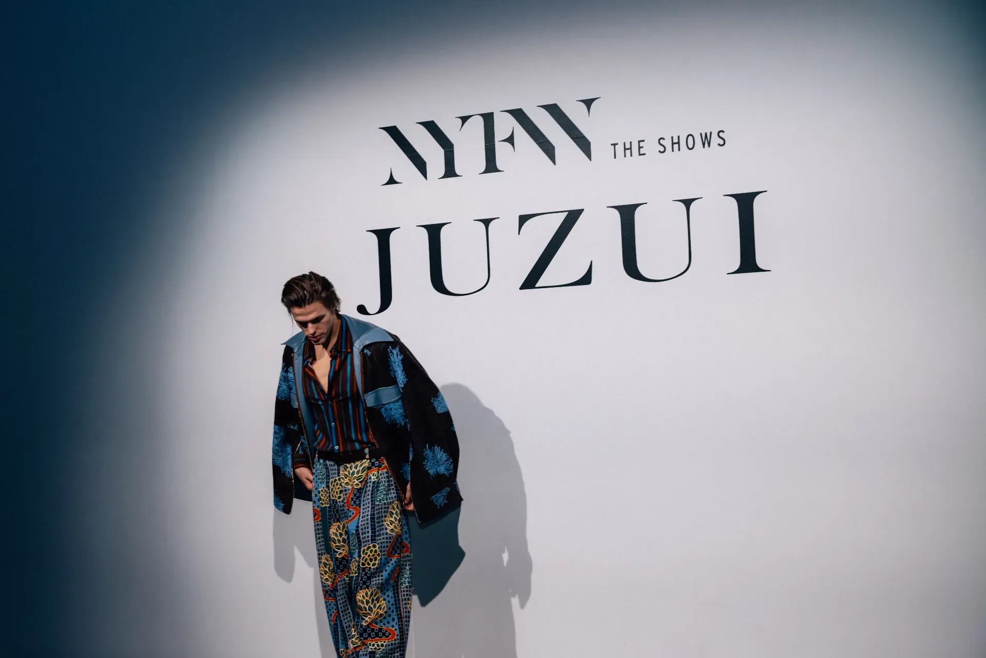 A man is standing in front of a wall with the word juzui on it.