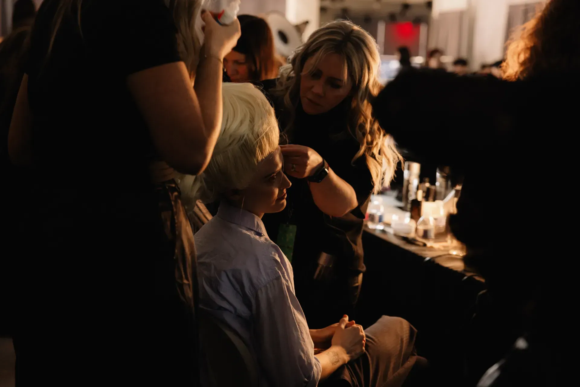 A woman is getting her makeup done by a makeup artist in a dark room.