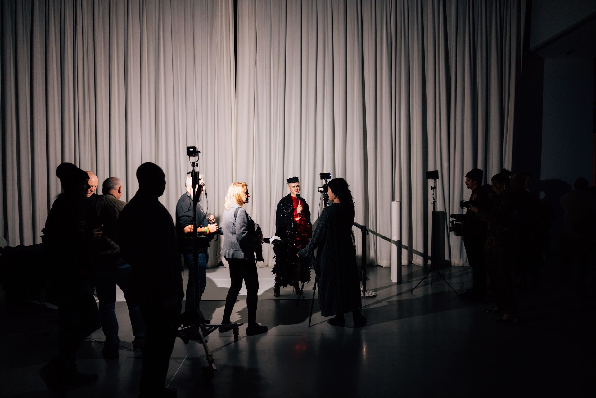 People filming someone in academic attire in front of a curtain backdrop. Lighting equipment is visible.