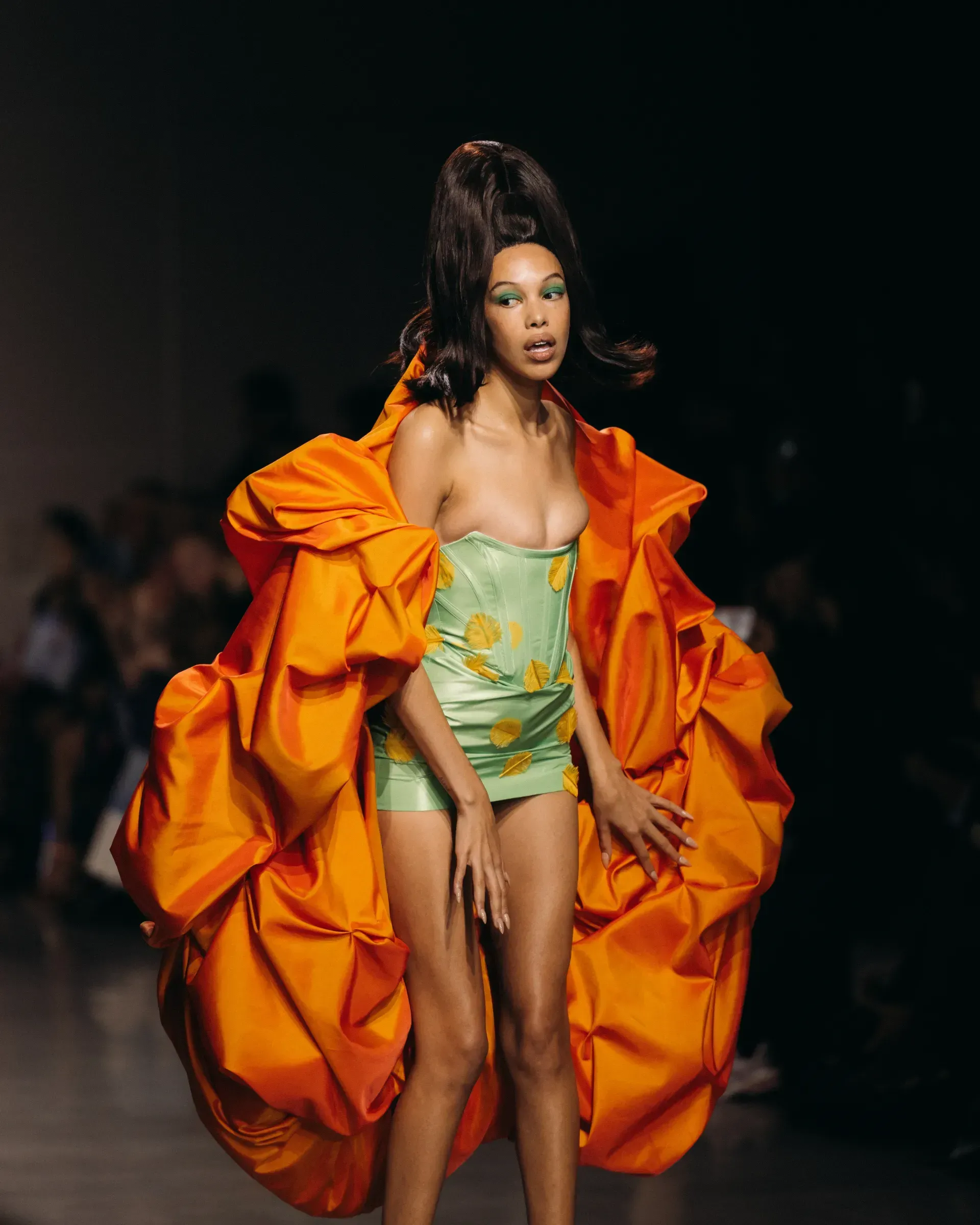 A woman is walking down a runway wearing an orange and green dress.